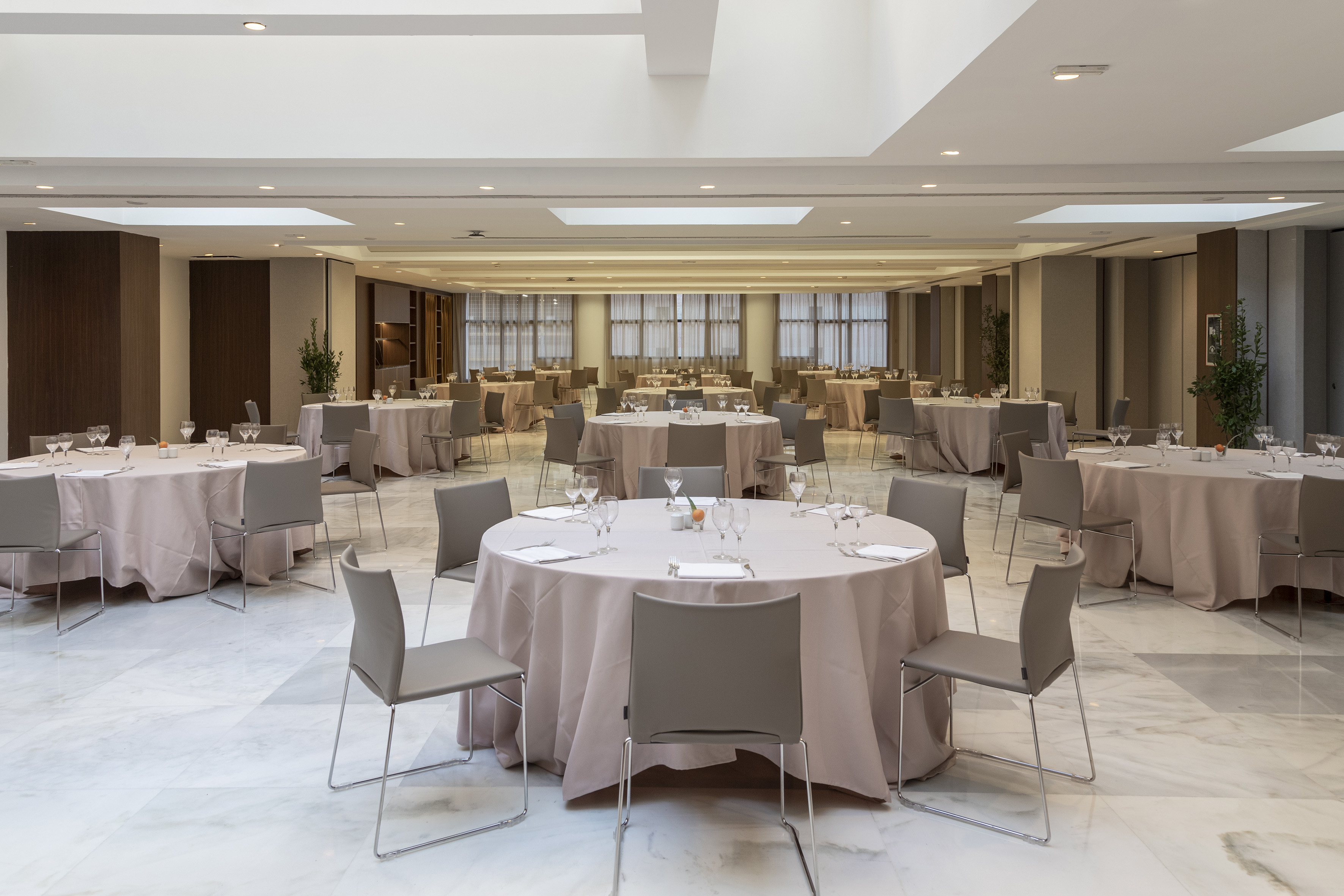 Spacious modern banquet hall with round tables set for an event, grey chairs.