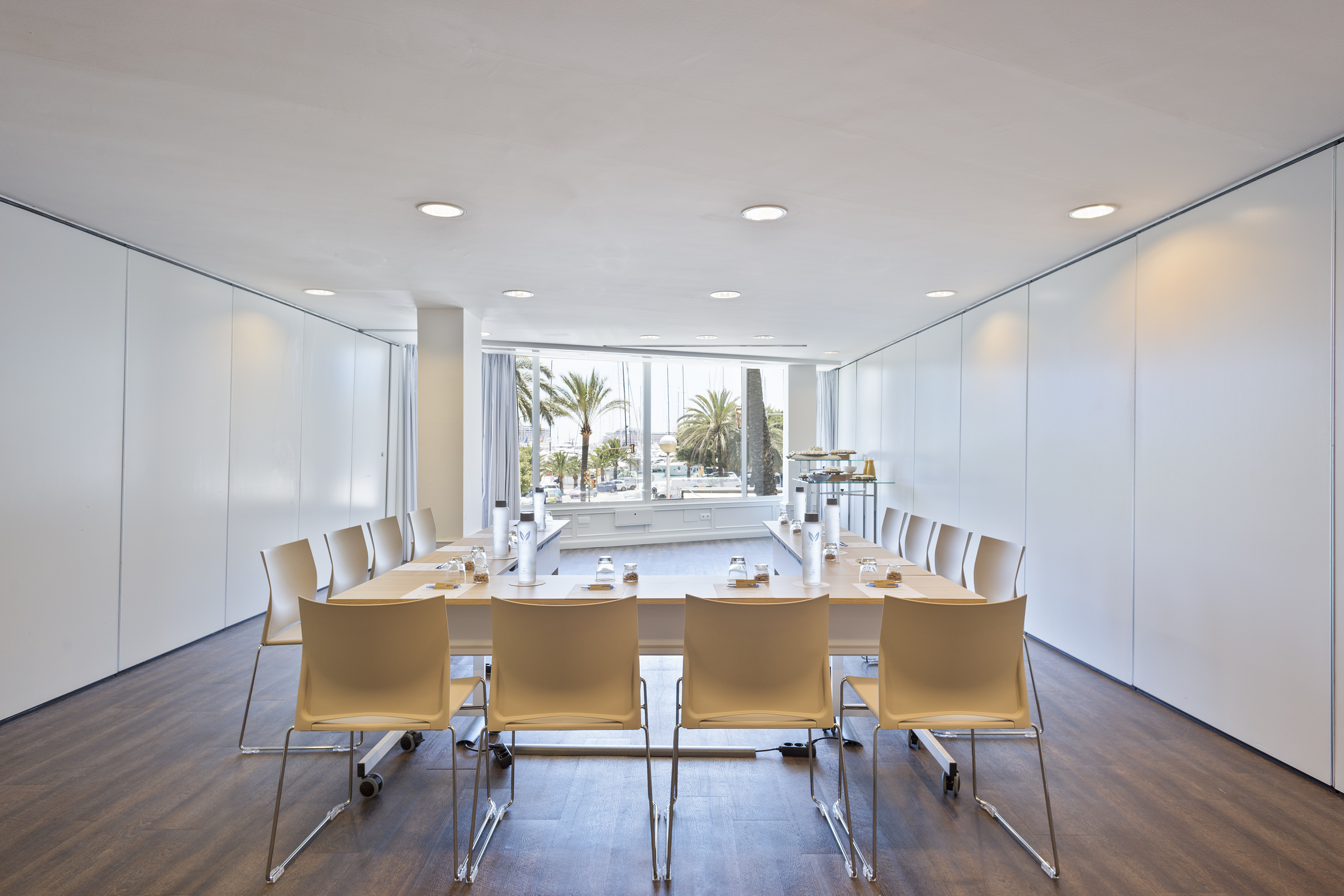 Modern conference room with U-shaped table, marina view, and palm trees outside.