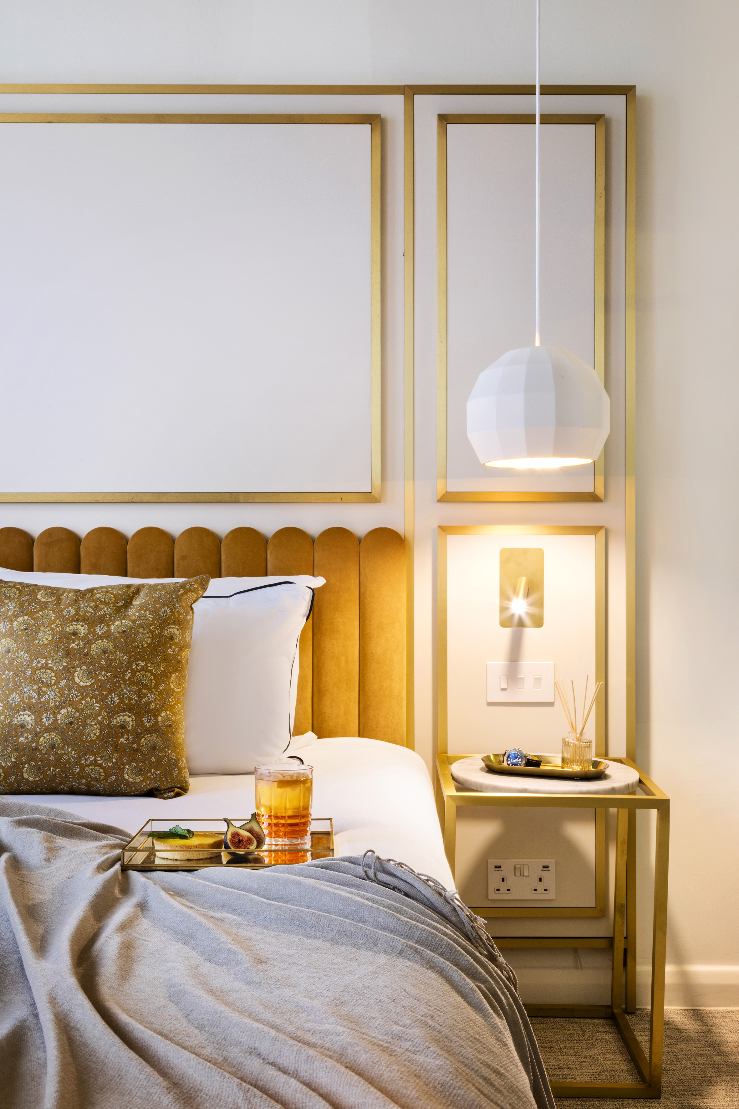 Luxury bedroom with gold headboard, modern geometric light, and bedside tray.