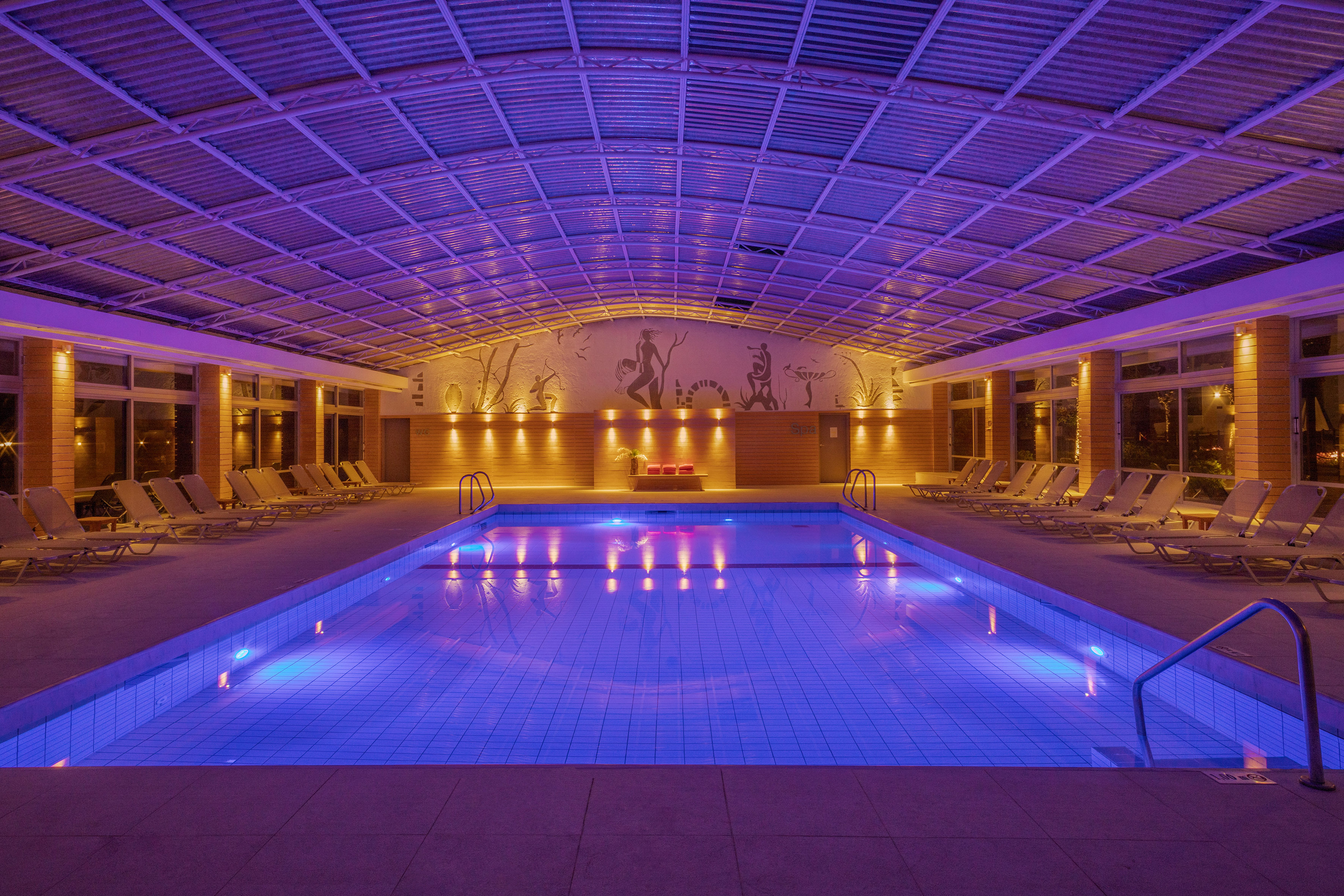 Indoor swimming pool with blue lights, sun loungers, and artistic wall mural.