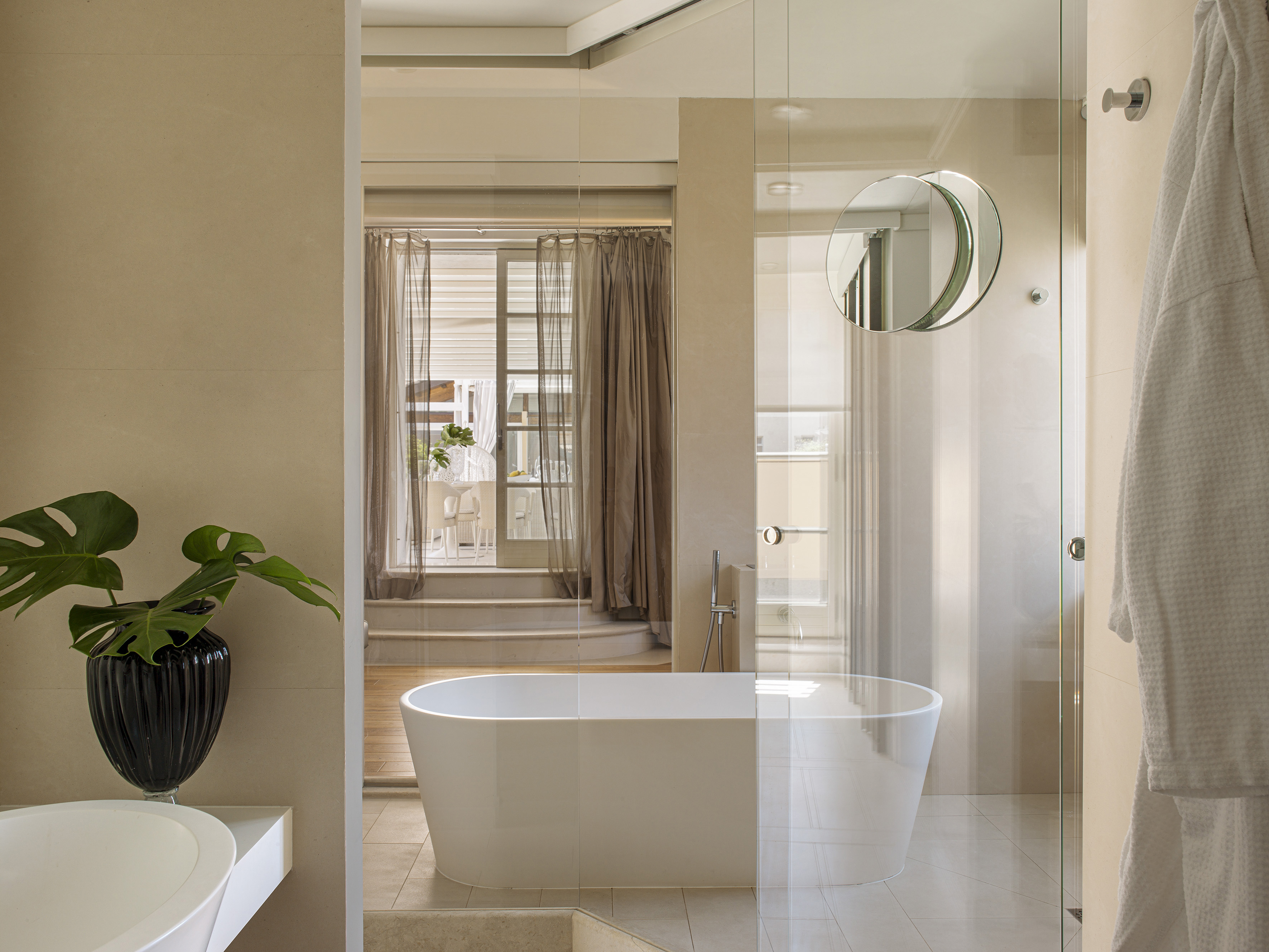 Modern bathroom with freestanding tub, glass shower, neutral tiles, green plant.