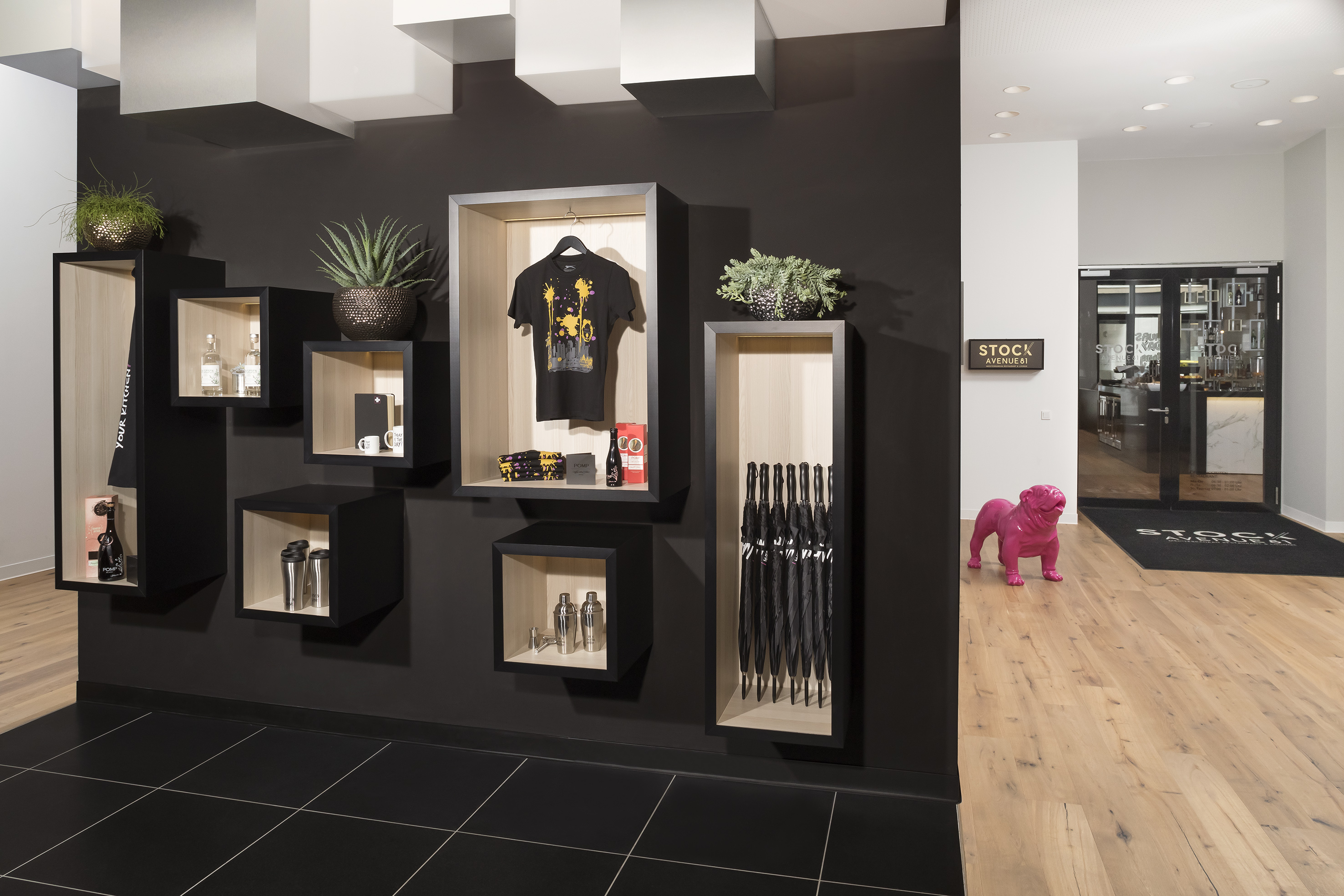 Modern black wall retail display with shelves, plants, and pink bulldog statue.