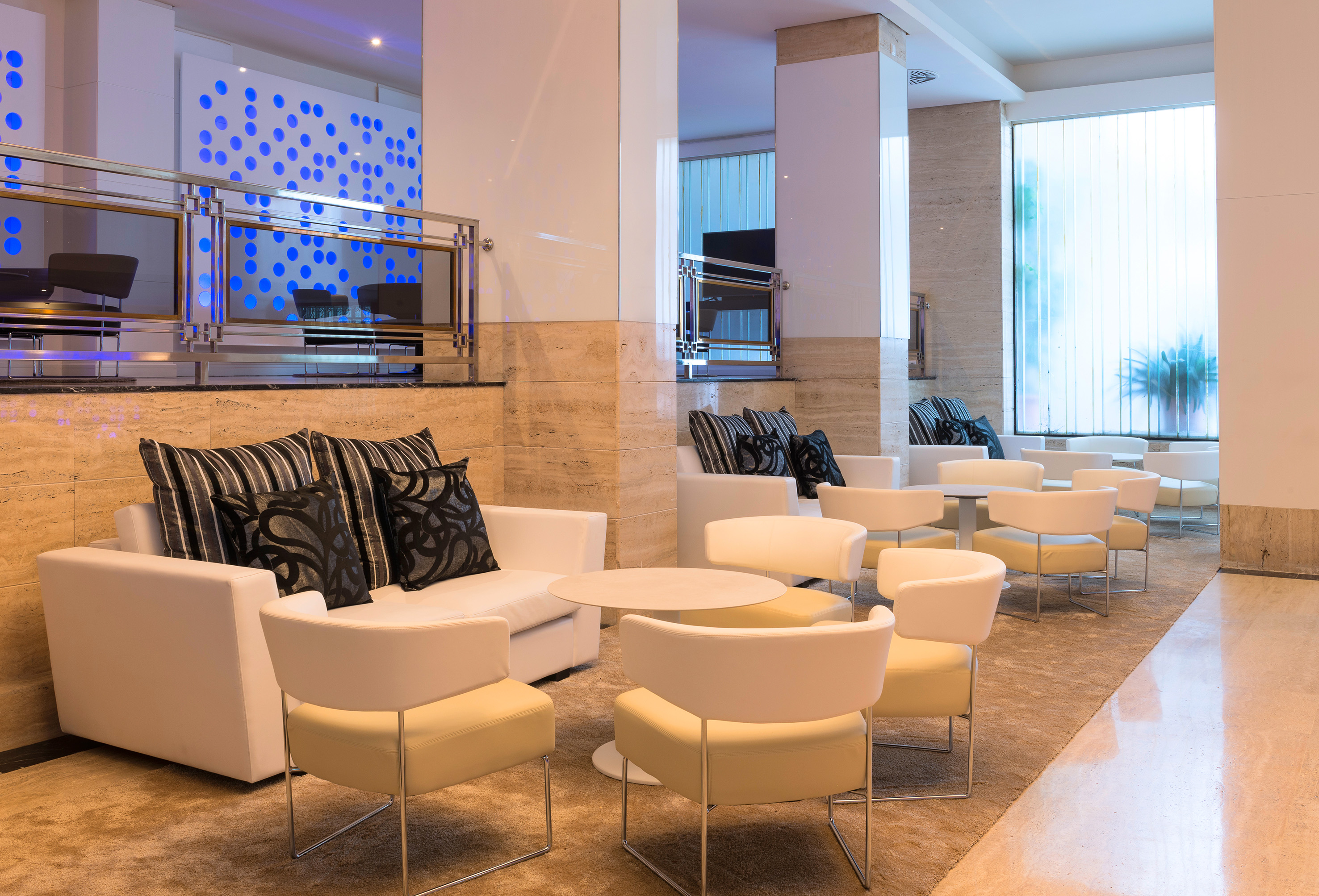 Modern hotel lounge with white sofas, beige chairs, and blue light wall.