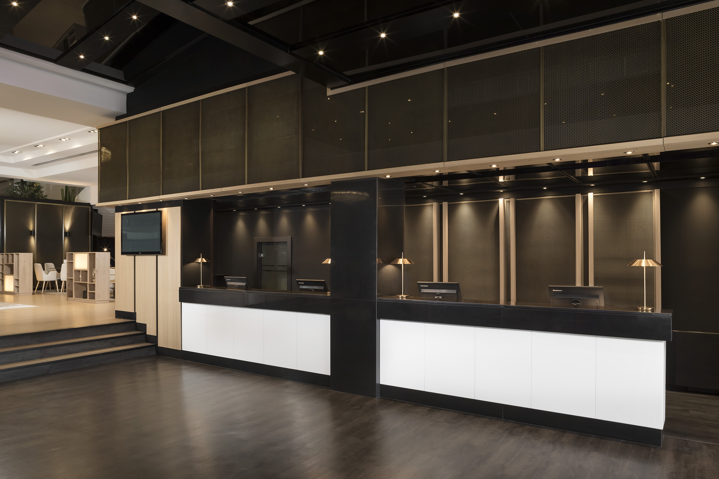 Modern hotel lobby with black and white reception desk and dark mesh paneling.