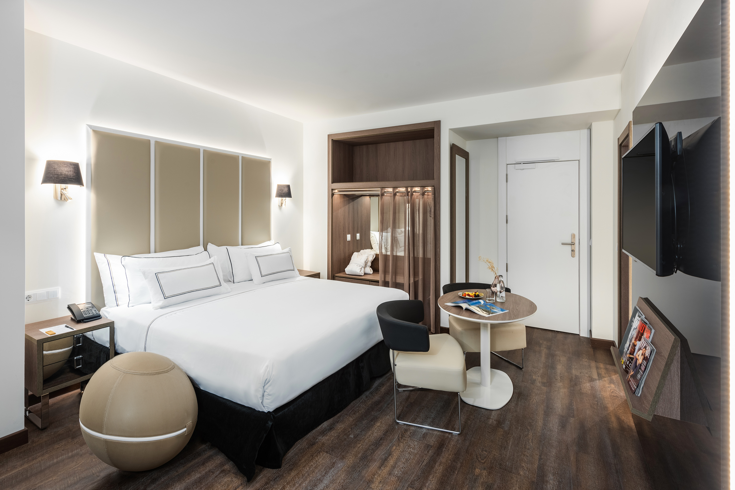 Modern hotel room with large bed, elegant headboard, wooden floor, and dining table.