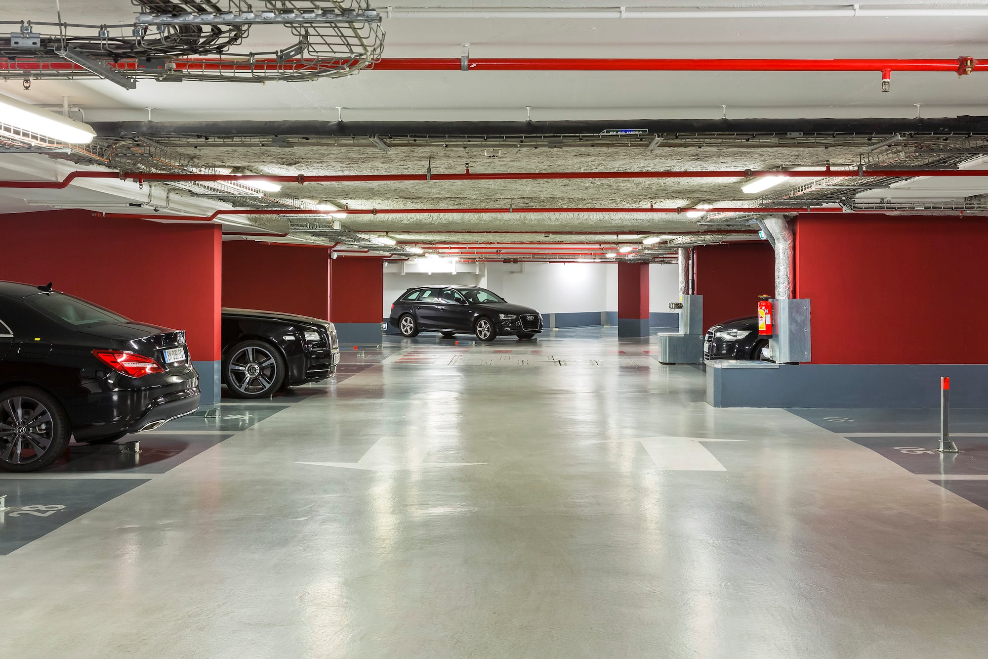 Underground parking garage with black cars, red walls, and concrete floor.