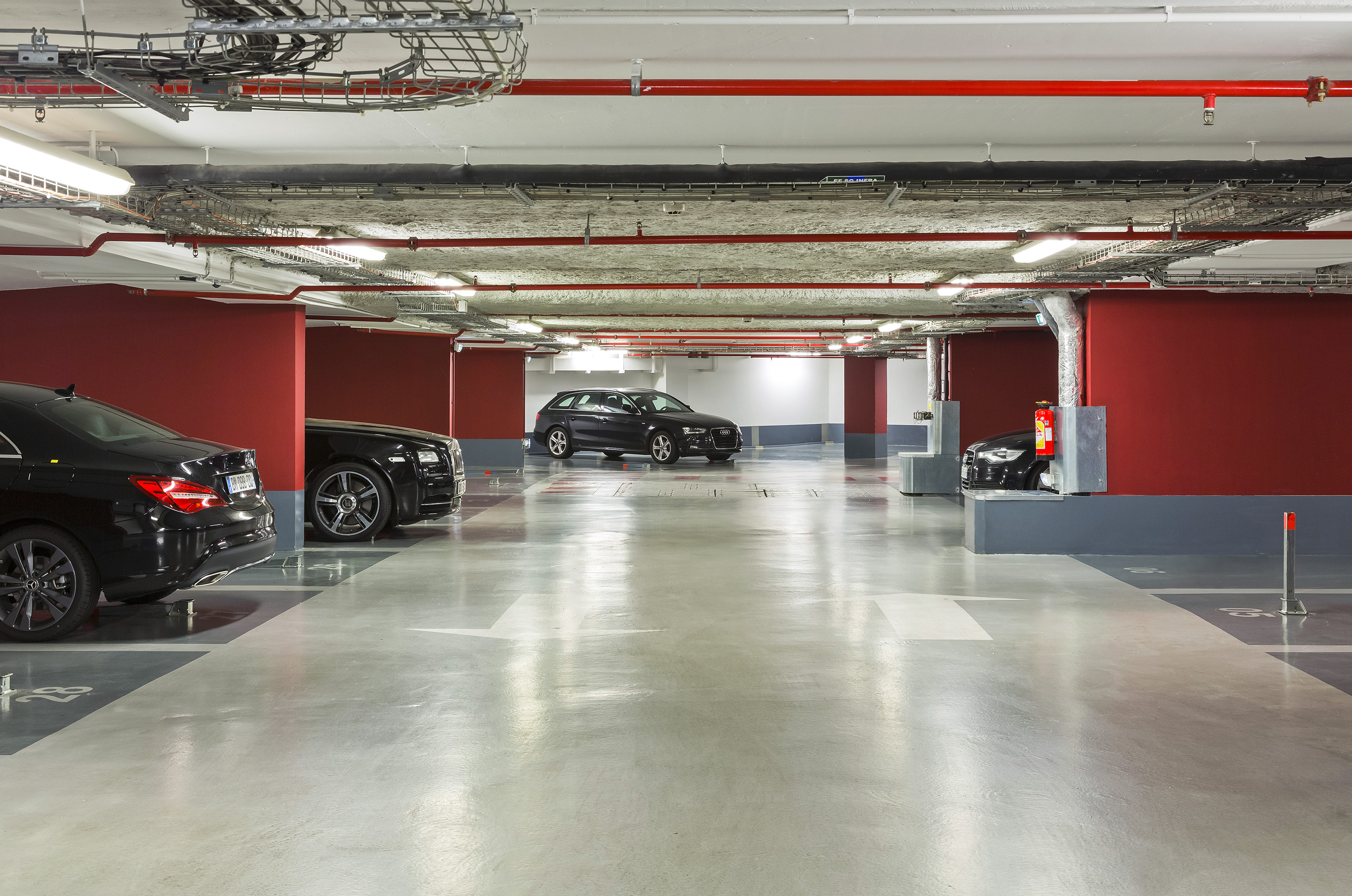 Underground parking garage with black cars, red walls, and concrete floor.