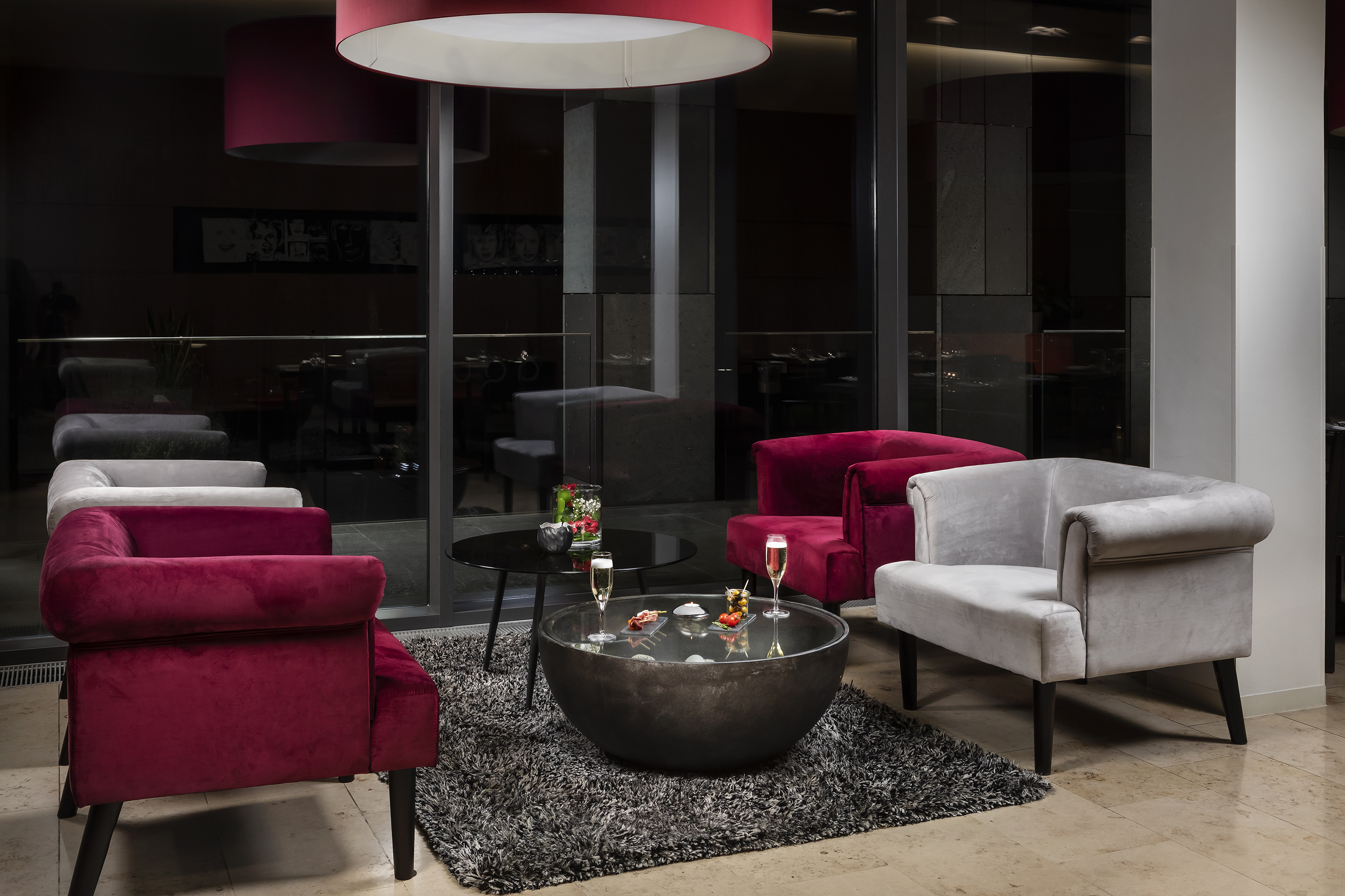 Modern hotel lounge with red and grey velvet armchairs, champagne, and appetizers.