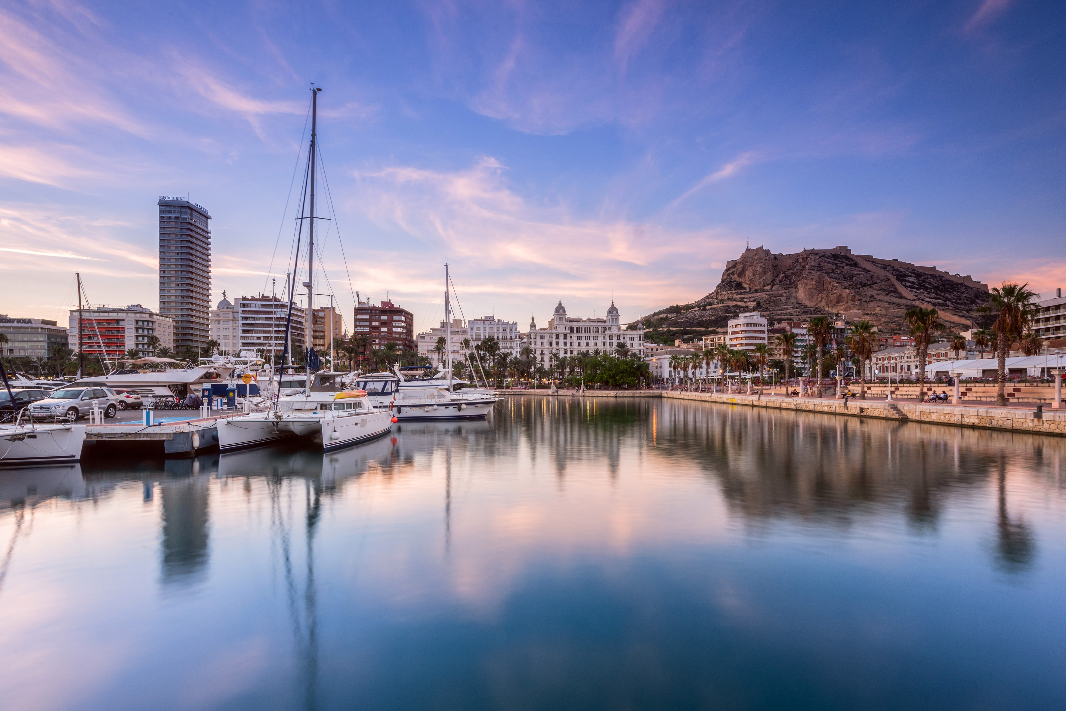 Alicante marina at sunset with city skyline and Santa Bárbara Castle.
