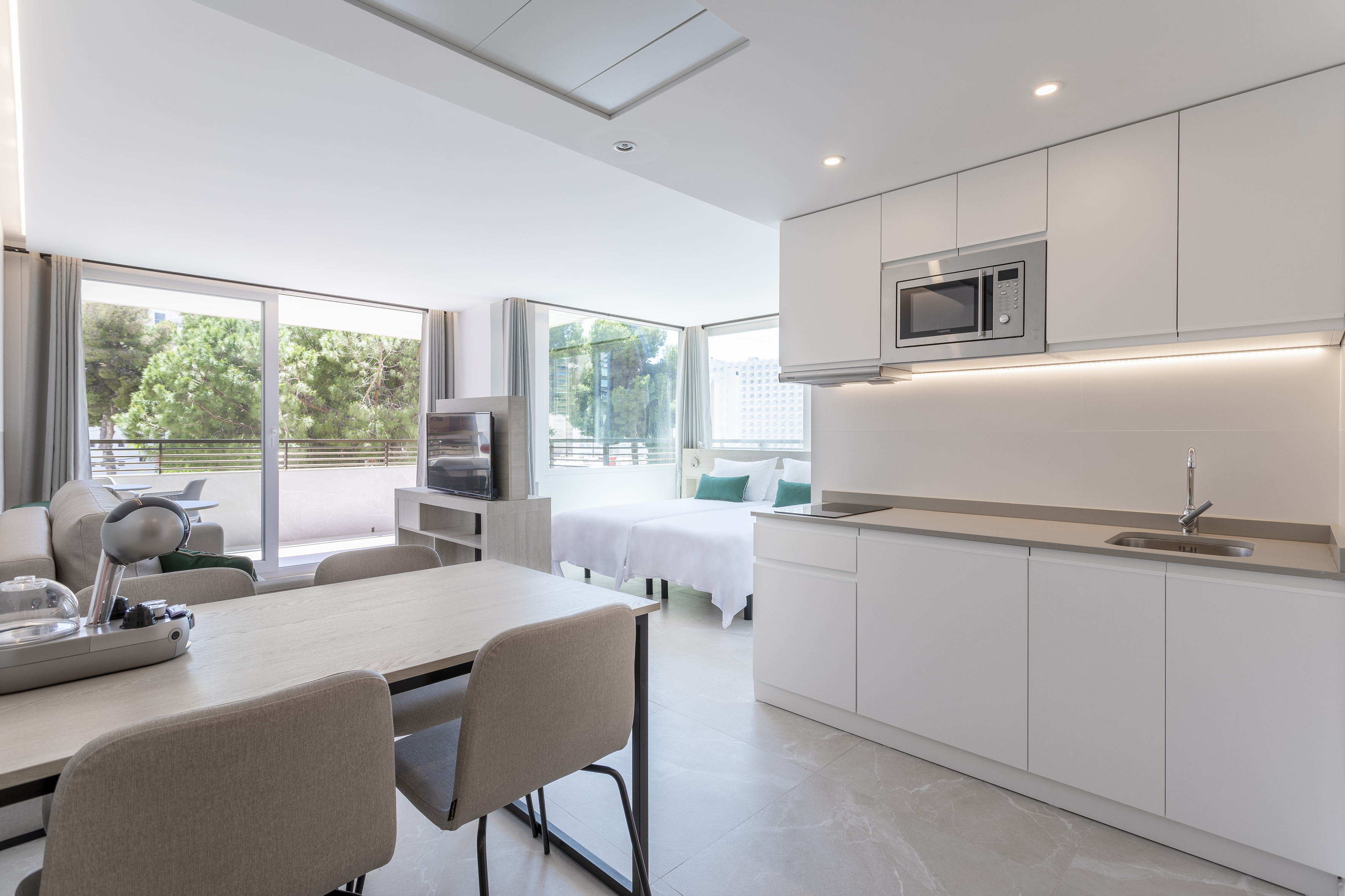 Modern hotel studio with kitchenette, dining, living area, twin beds, balcony.