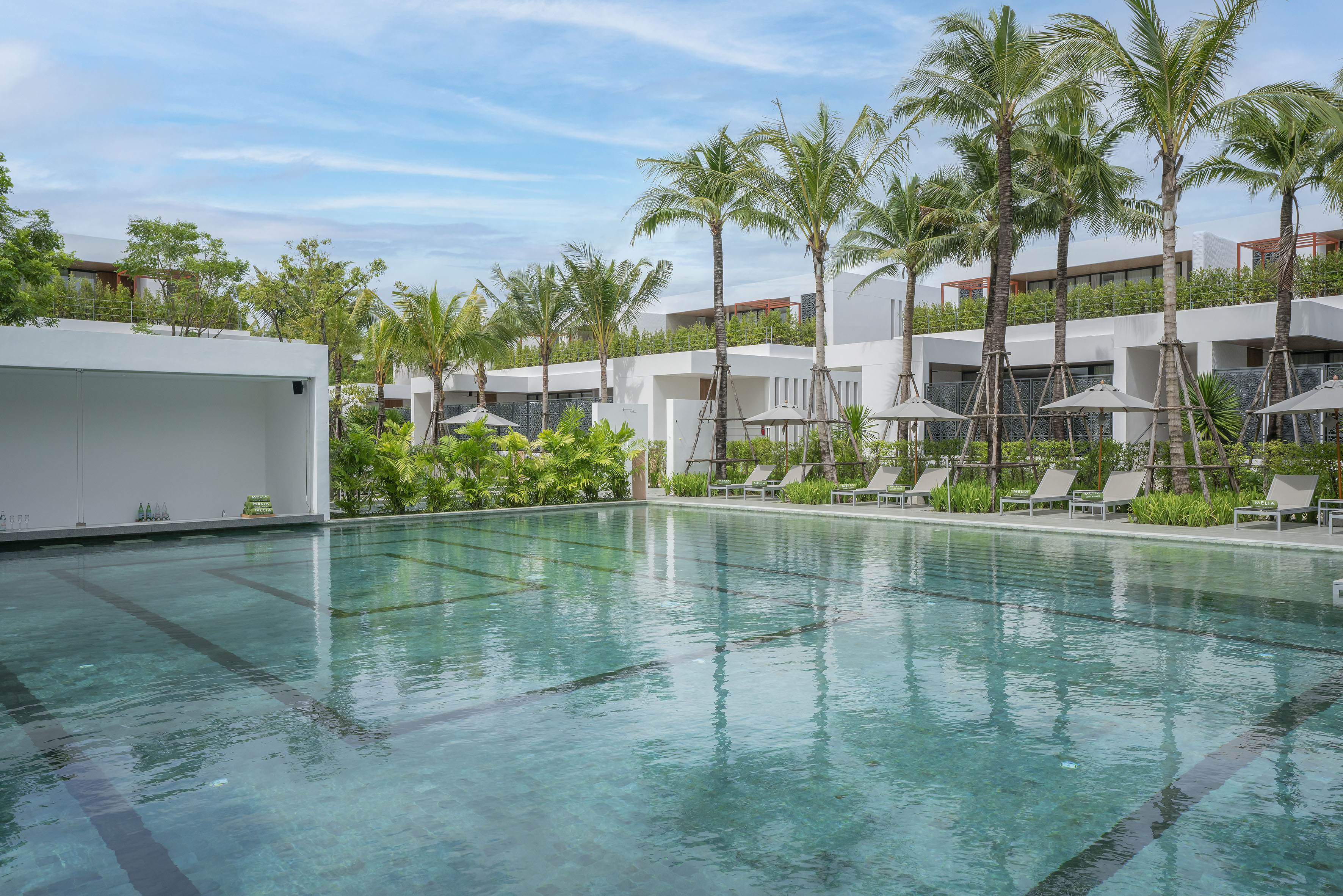 Modern resort pool, palm trees, and white hotel buildings with loungers.