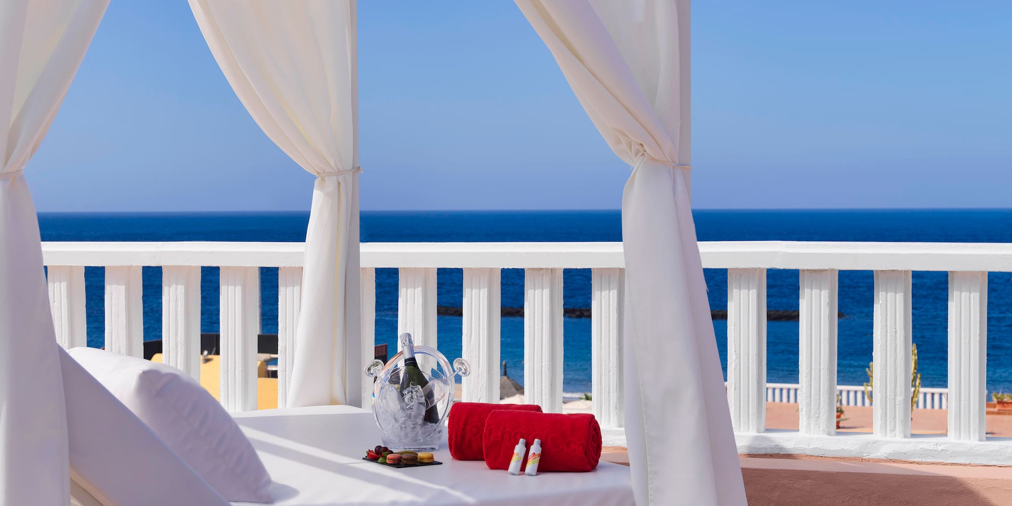 a white canopy bed with a glass vase and towels on it