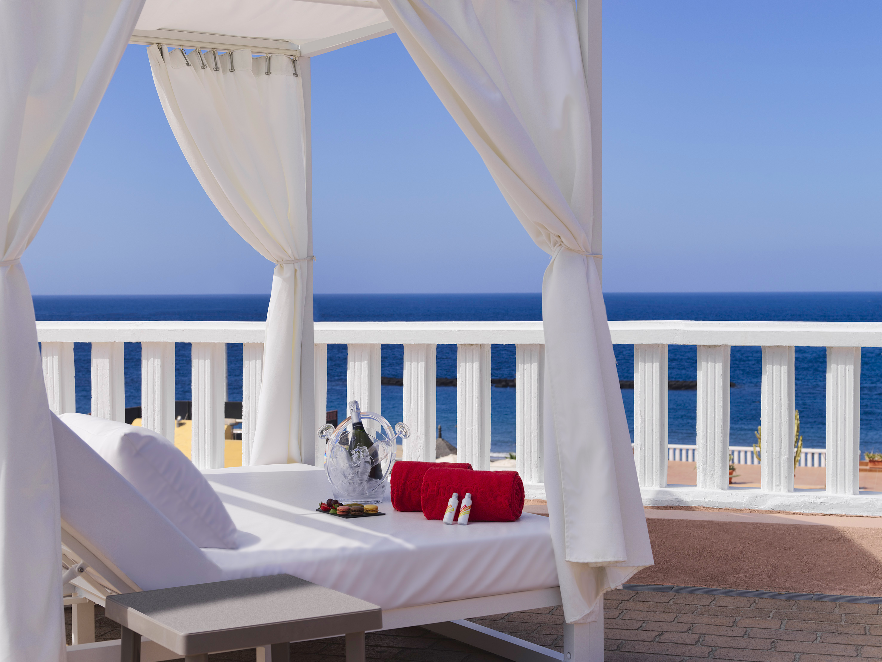 White canopy bed with champagne and red towels overlooking the blue ocean.