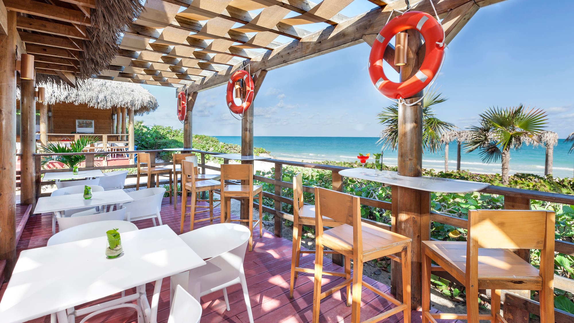 a patio with tables and chairs and a beach view