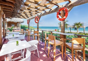 a patio with tables and chairs and a beach view