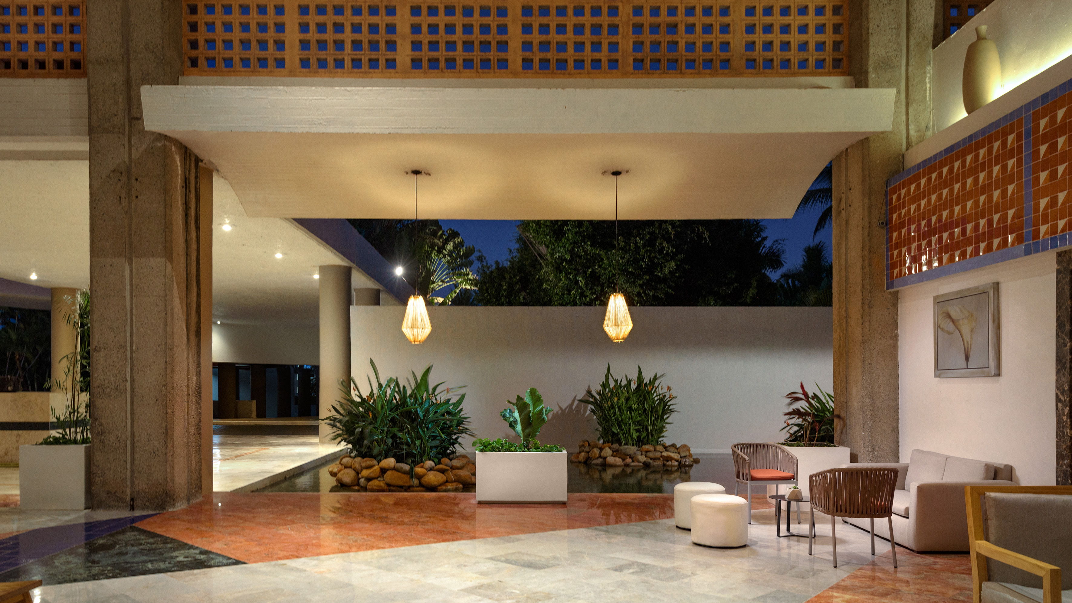 Modern hotel lobby with contemporary seating, lush indoor plants, and warm lighting.