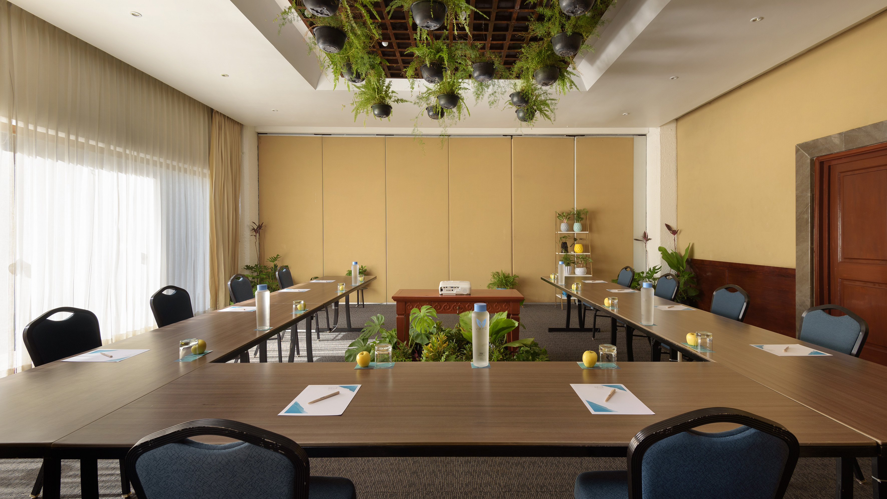U-shaped conference room with tables, chairs, and hanging plants decor.