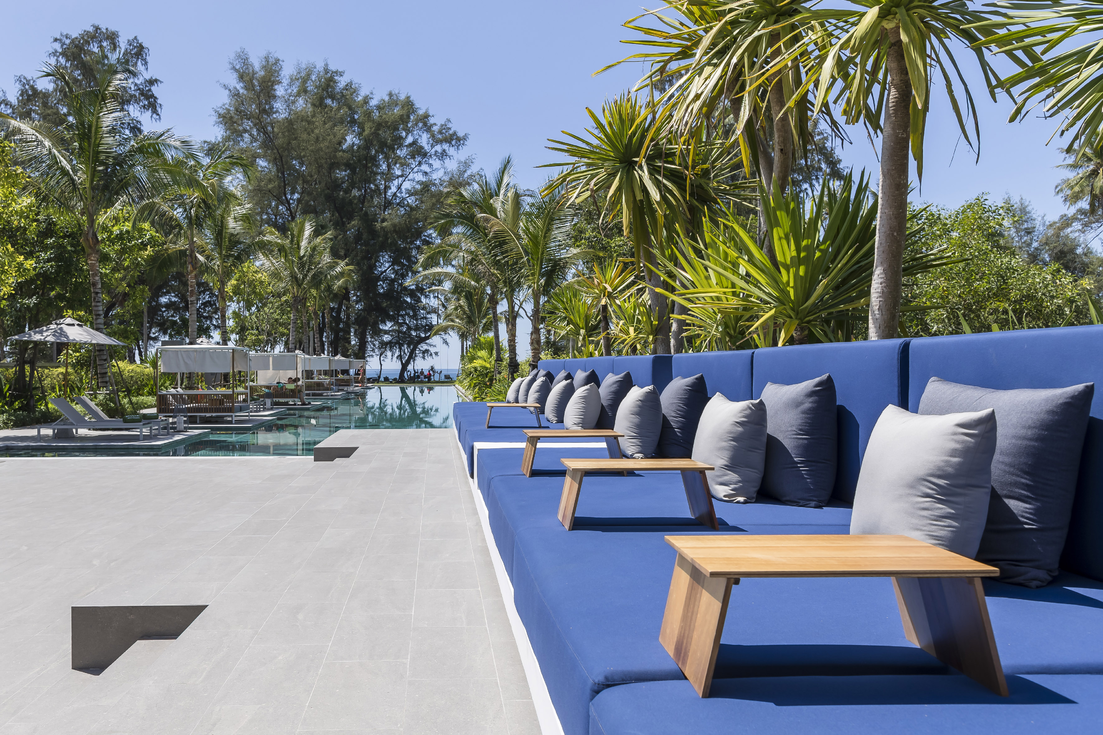 Blue daybeds with wooden tables, palm trees, and swimming pool at a tropical resort.