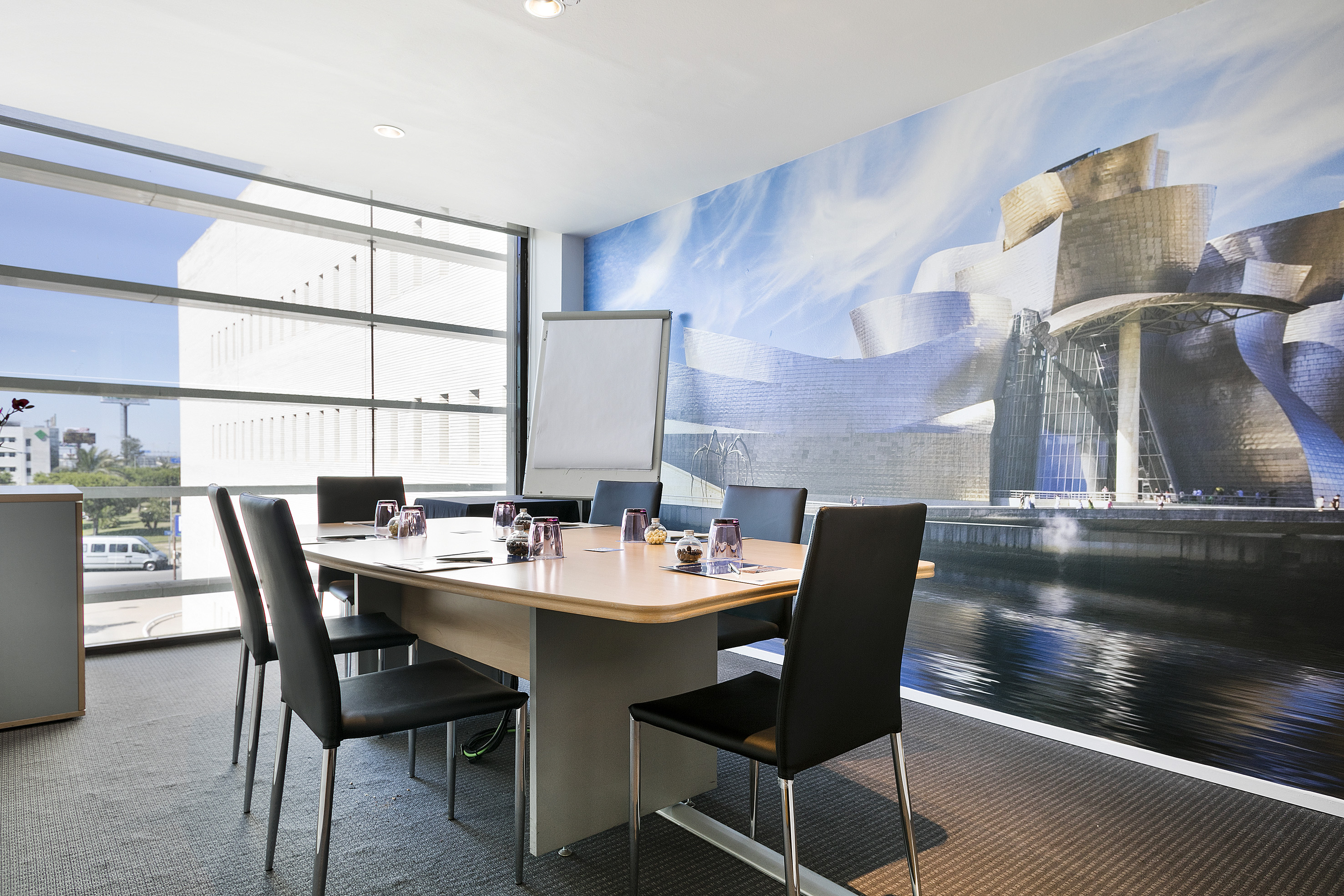 Conference room with Guggenheim Bilbao wall mural, meeting table, city view.
