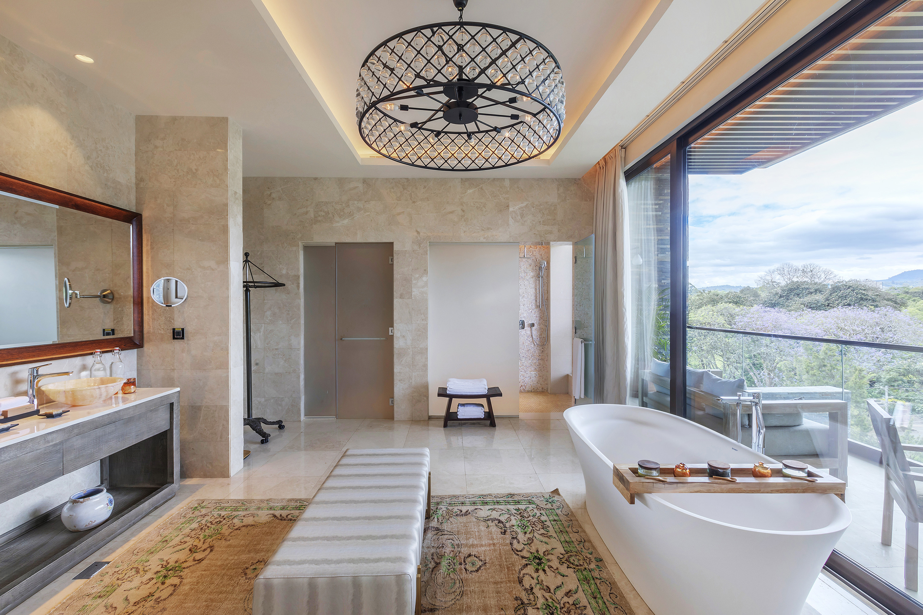 Modern luxury bathroom with freestanding tub, chandelier, and panoramic view balcony.
