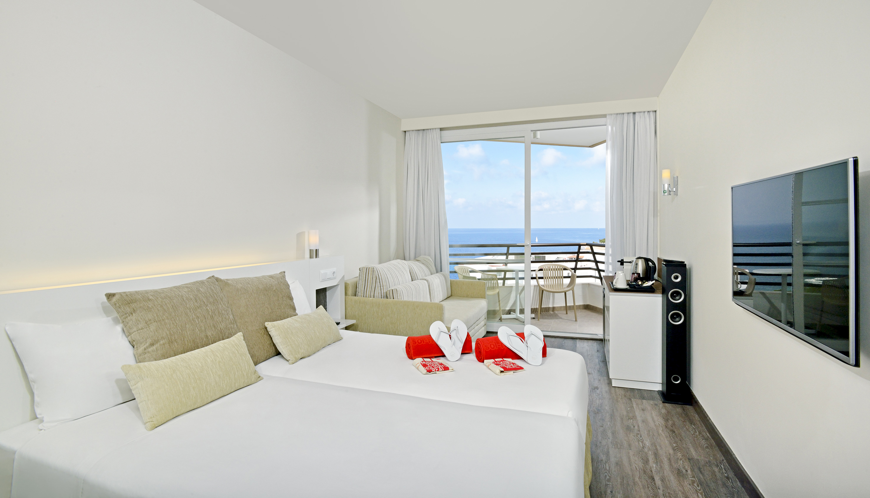 Hotel room with twin beds, ocean view balcony, sofa, and TV.