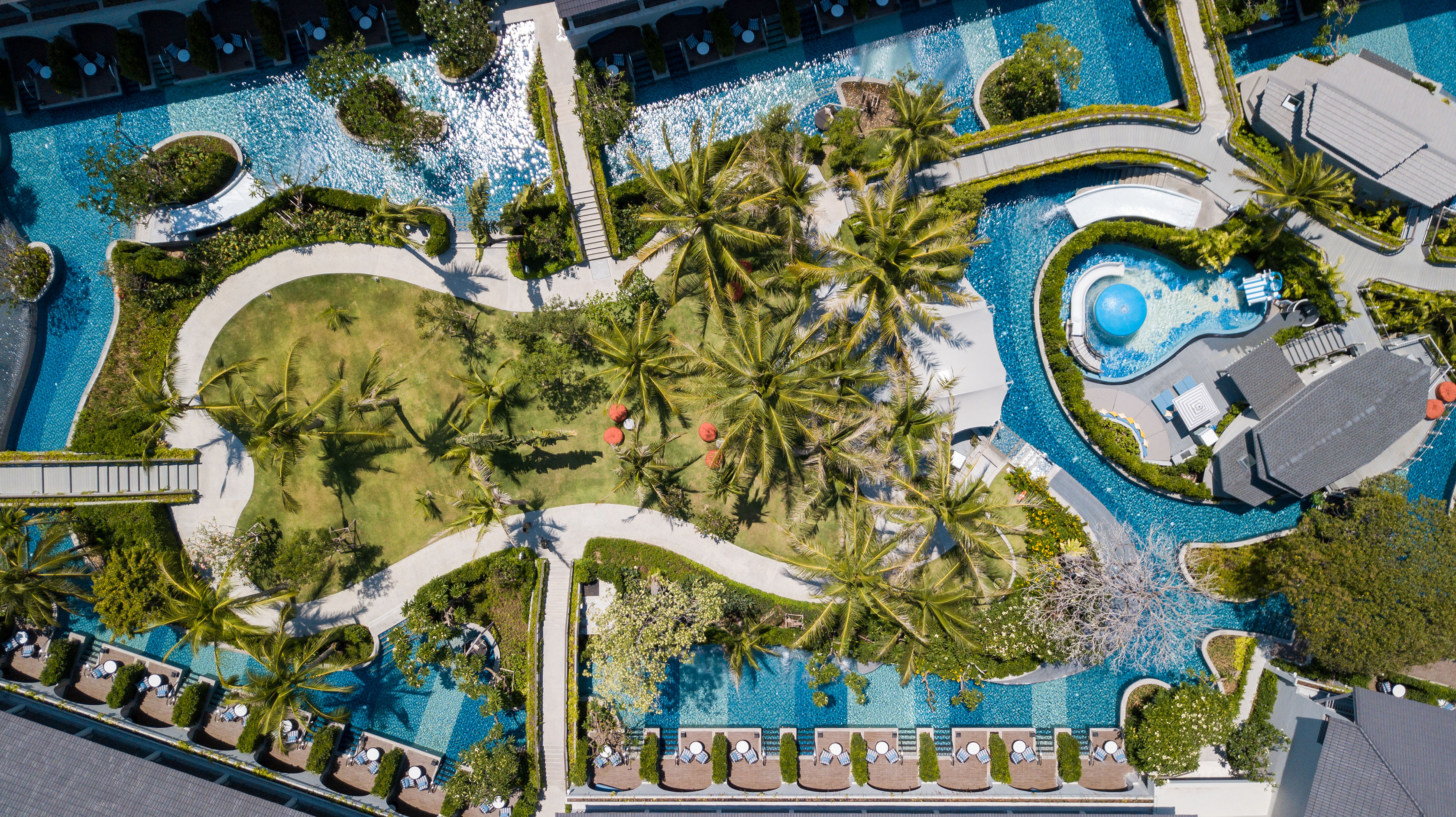 Aerial: tropical resort with winding pools, palm trees, and green gardens.