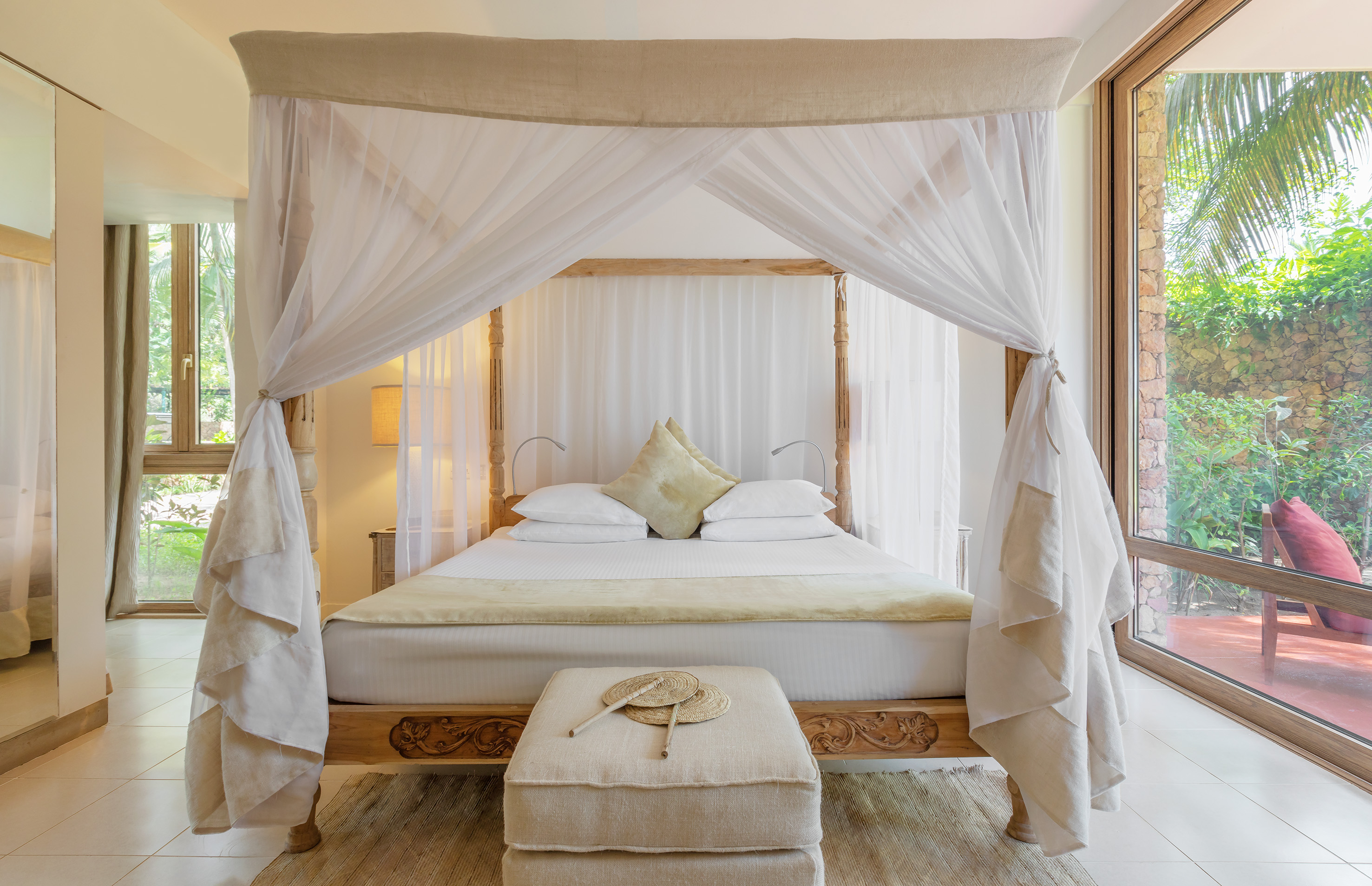 Tropical bedroom with elegant four-poster canopy bed and lush outdoor views.