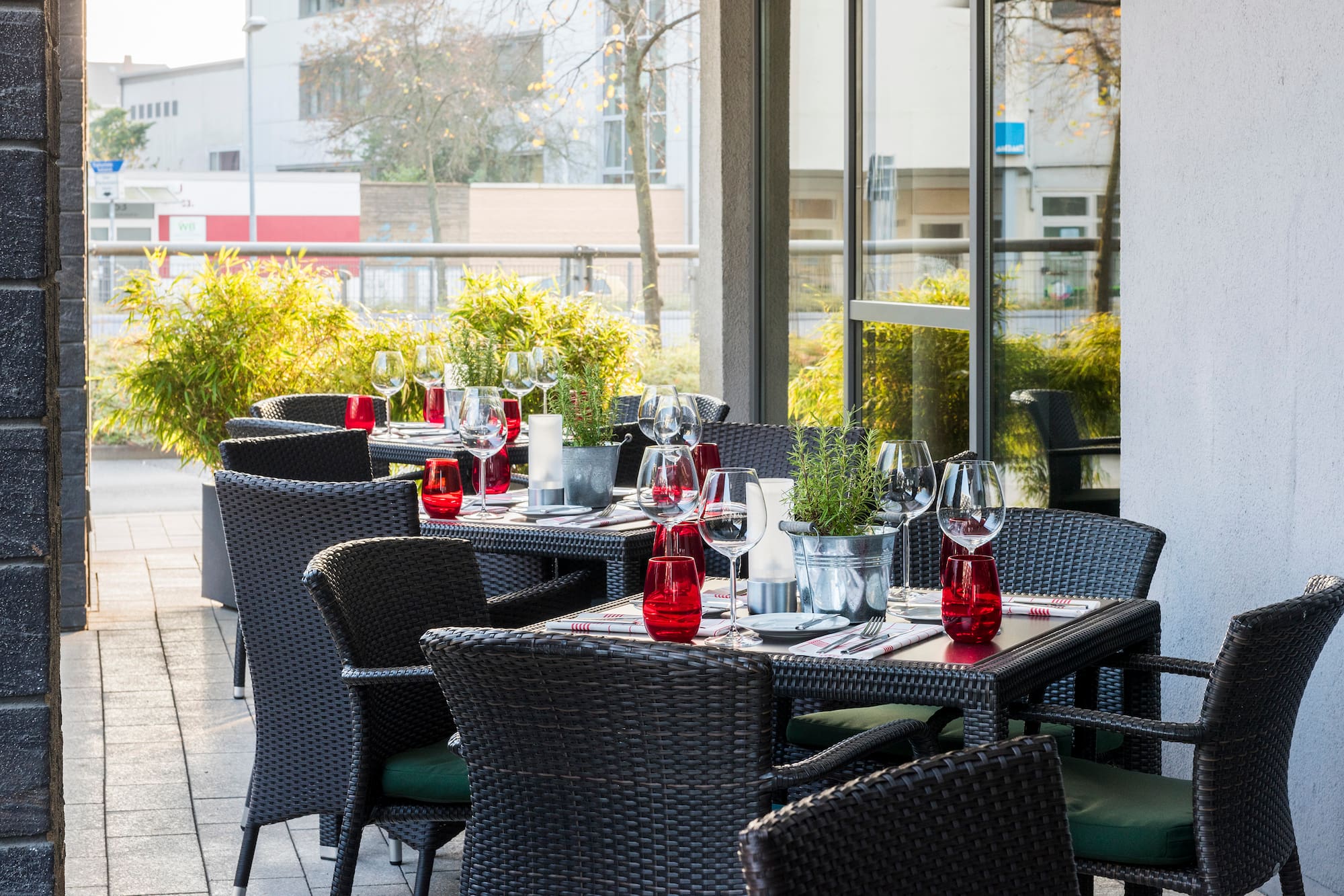 Restaurant patio dining area with set tables, dark chairs, red glasses.