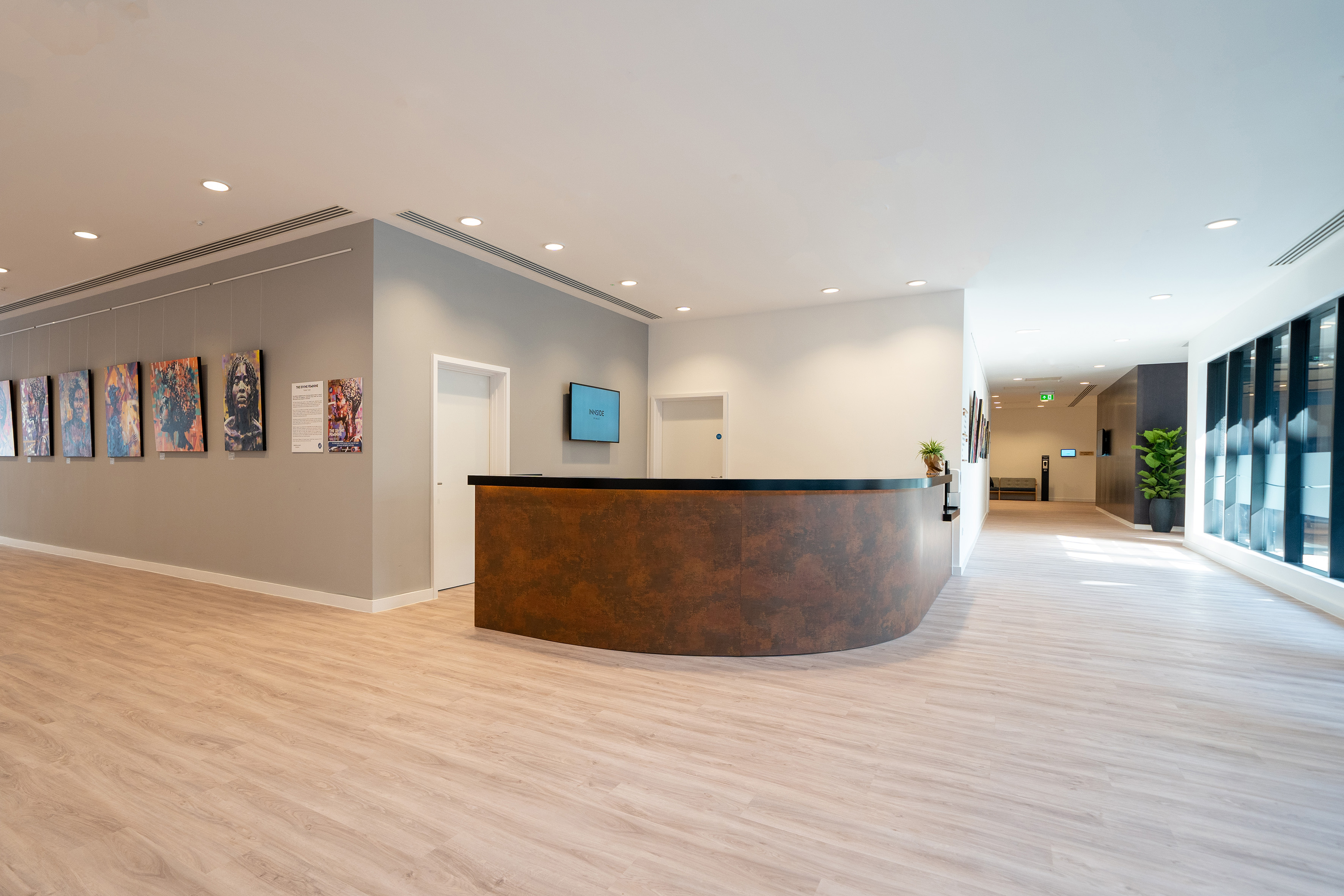 Modern hotel reception with dark curved desk, colorful art wall, light wood floor.