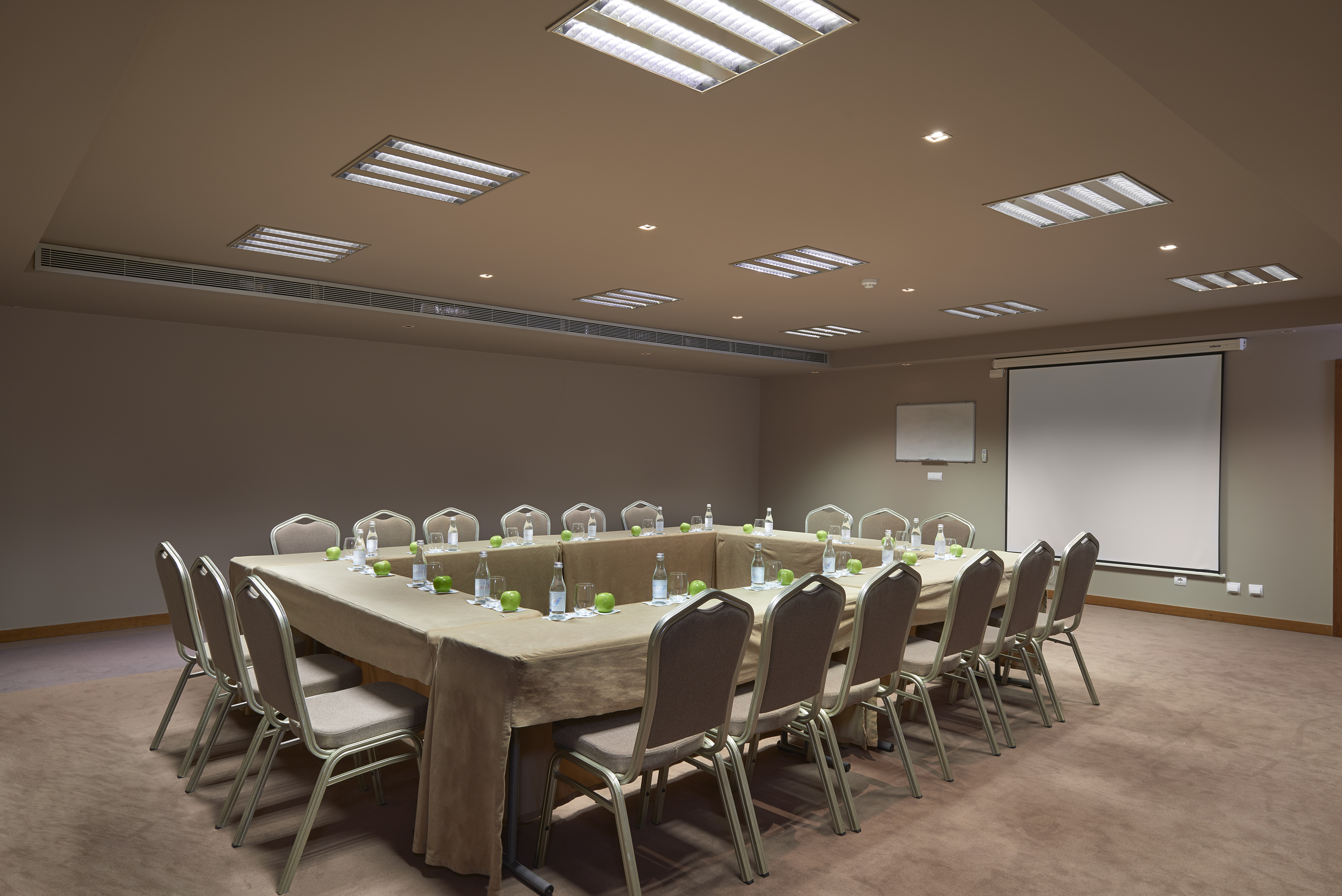 U-shaped conference room setup with projector screen, chairs, and table settings.