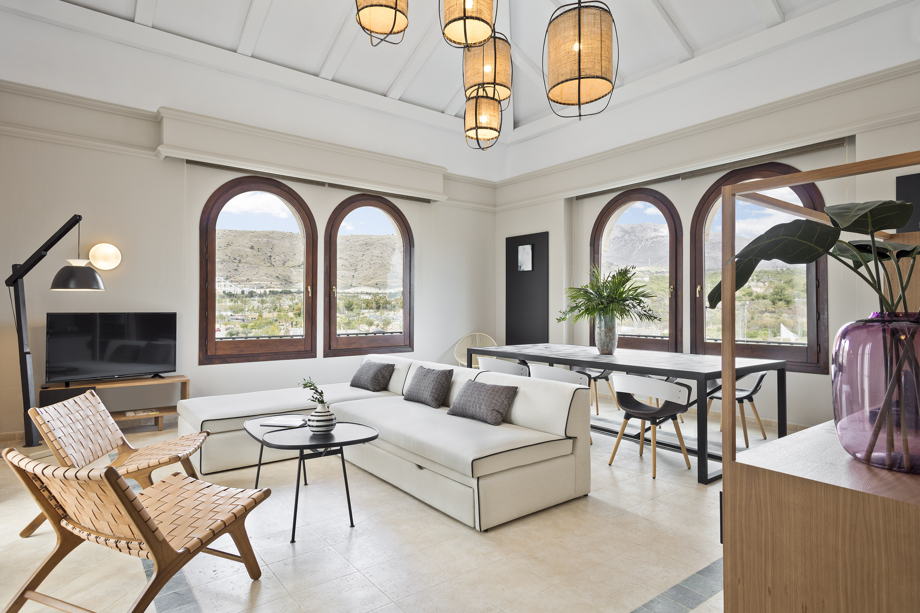 Living & dining room with white sofa, arched windows, mountain view, and rustic lights.