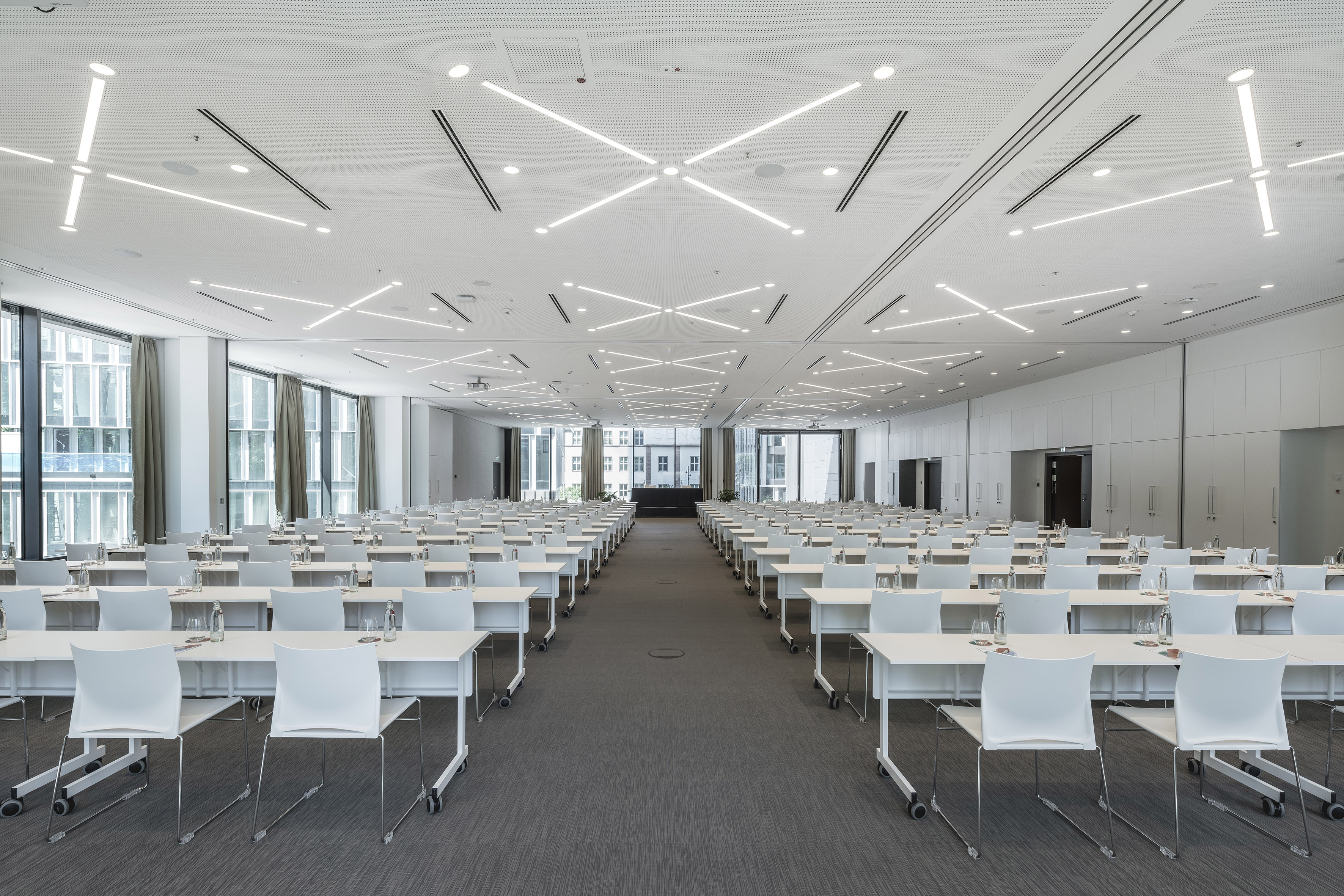 Empty modern meeting room with rows of white tables and chairs for a conference.