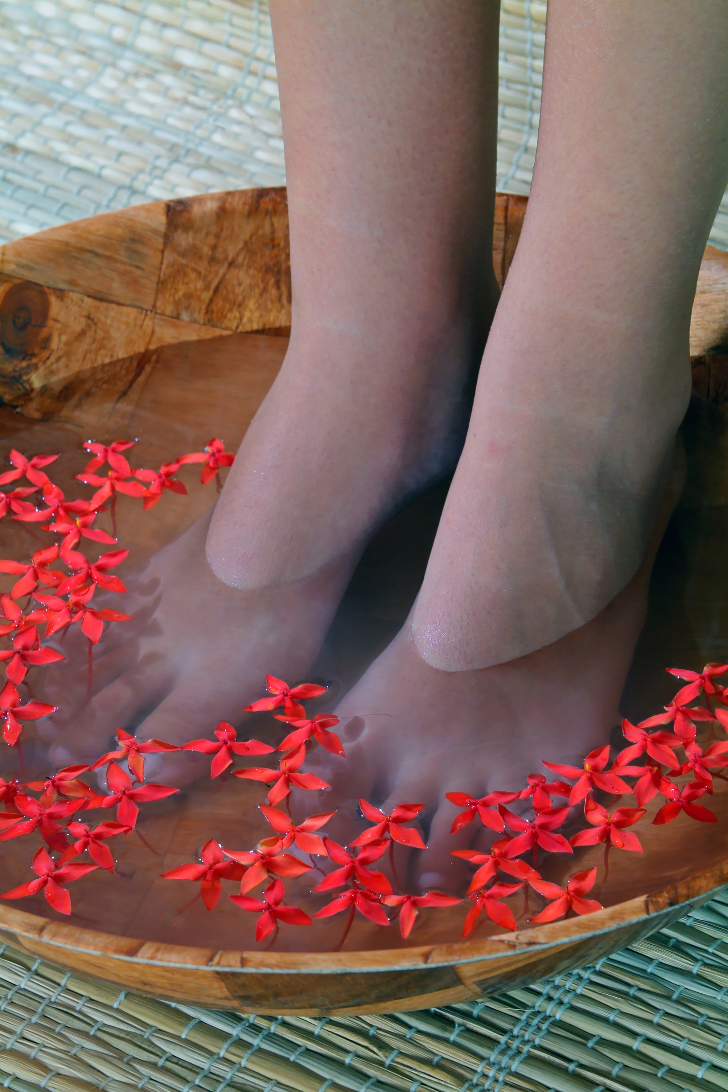 a person's feet in a bowl of water with red flowers