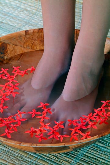 a person's feet in a bowl of water with red flowers