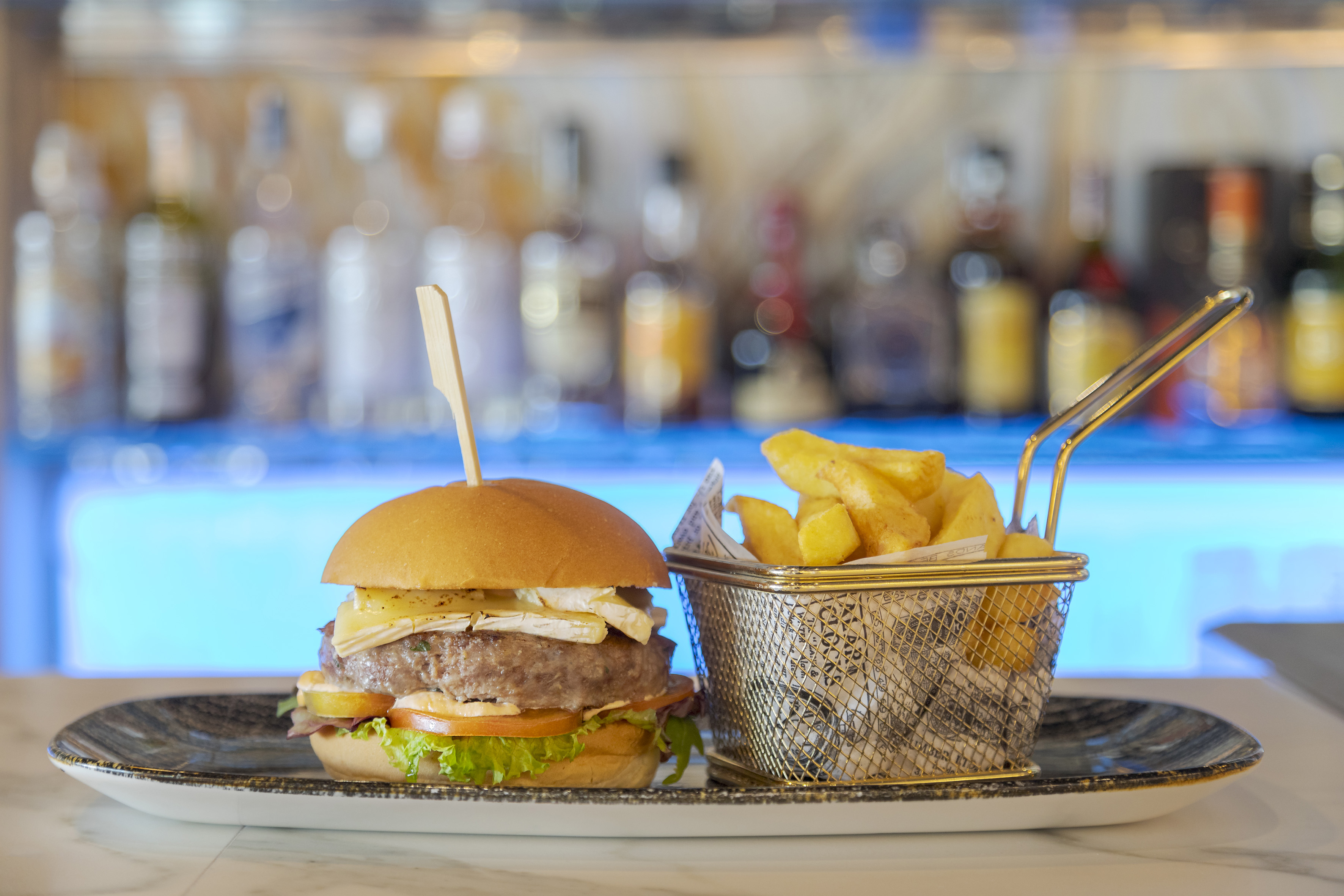 Gourmet burger with brie cheese and golden fries served on a plate at a bar.