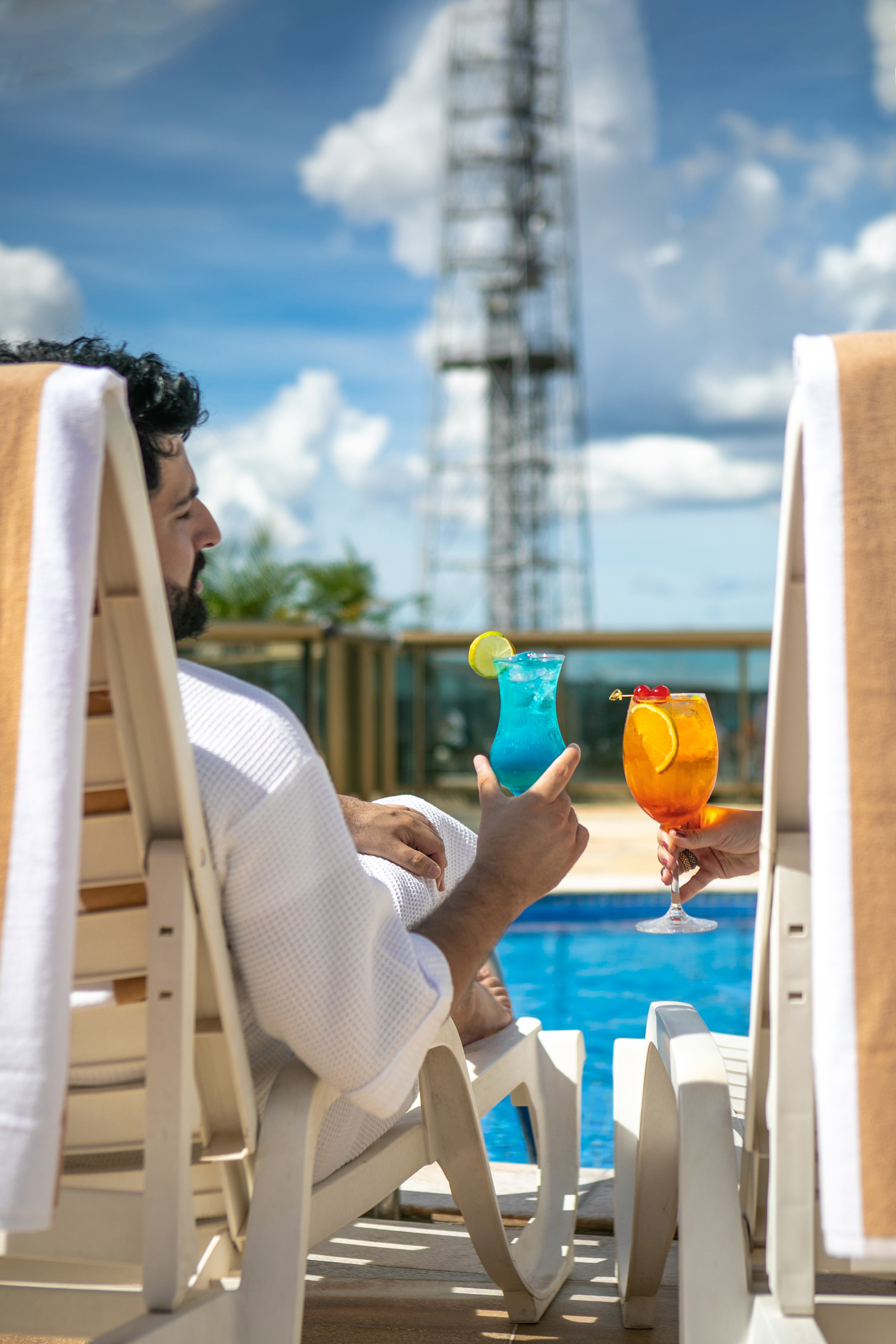 Two people enjoying colorful cocktails by a sunny resort pool.