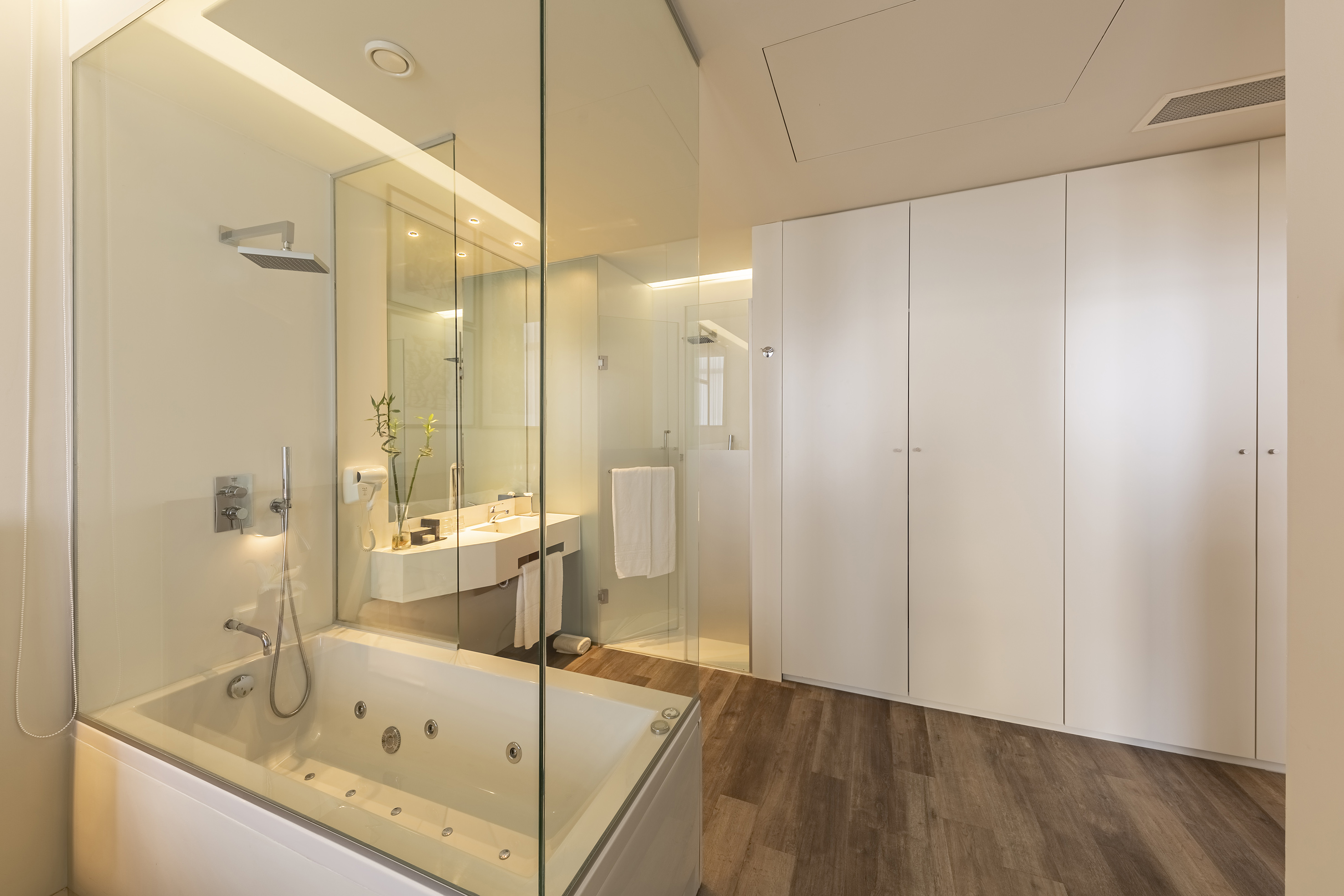 Modern luxury bathroom with jacuzzi tub, glass shower, vanity, and white cabinets.