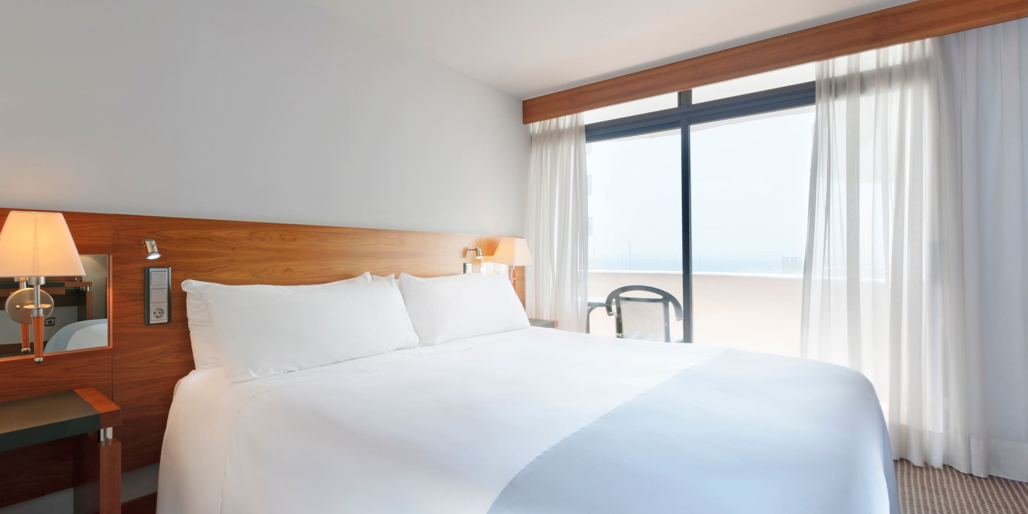 a bed with white sheets and a lamp next to a window