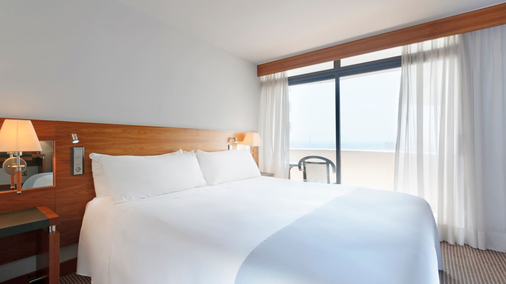 a bed with white sheets and a lamp next to a window