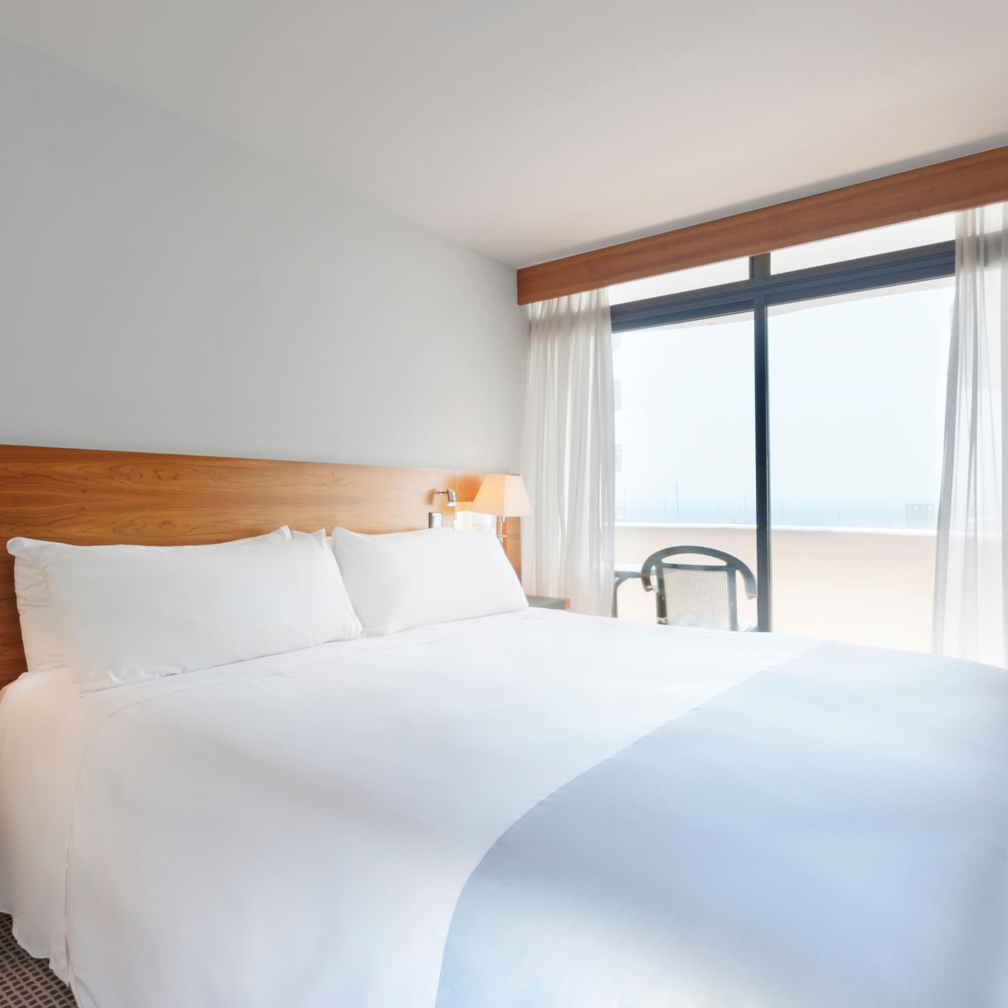 a bed with white sheets and a lamp next to a window