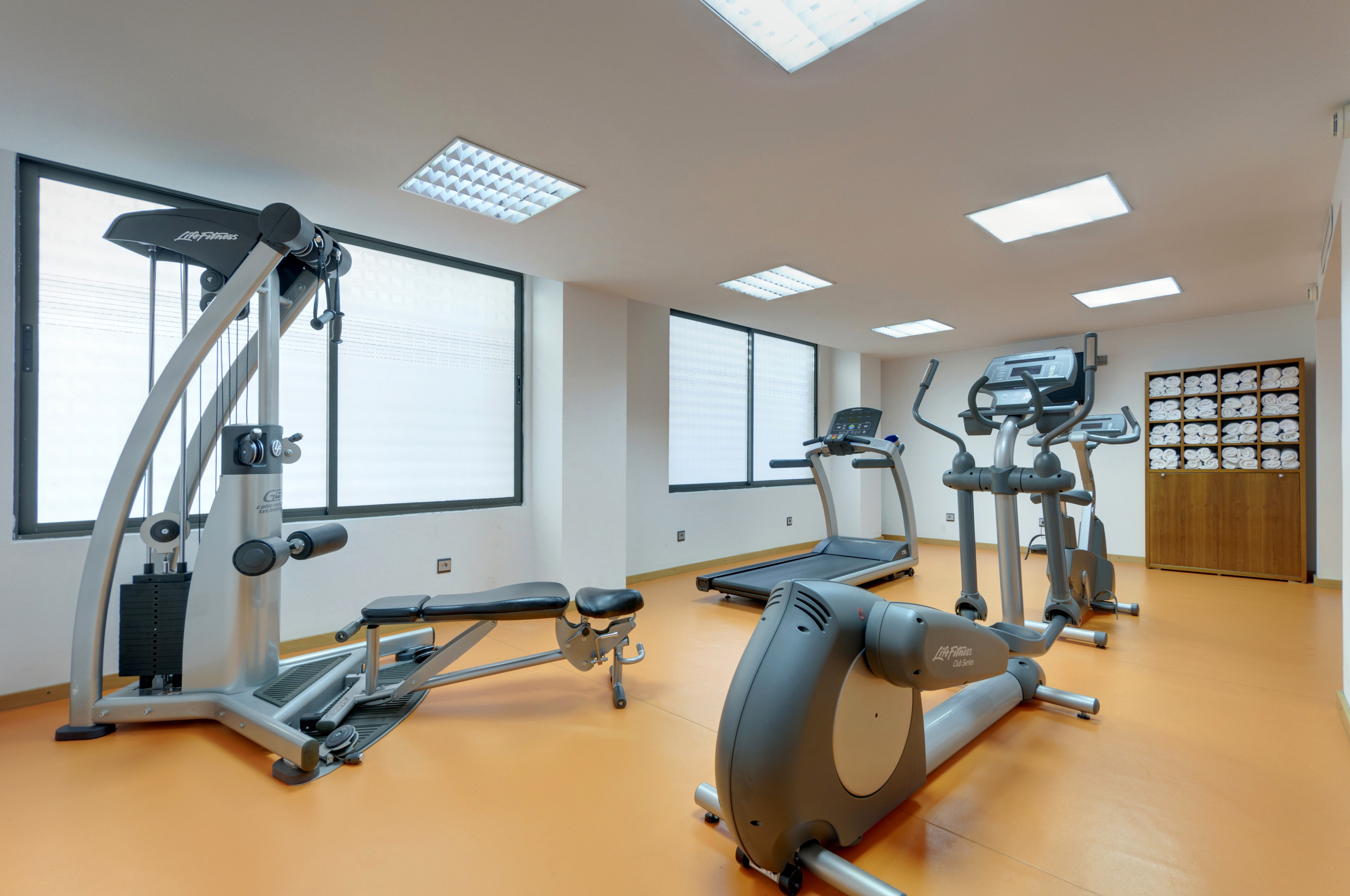 Bright gym featuring cardio machines, strength equipment, and neatly folded towels.