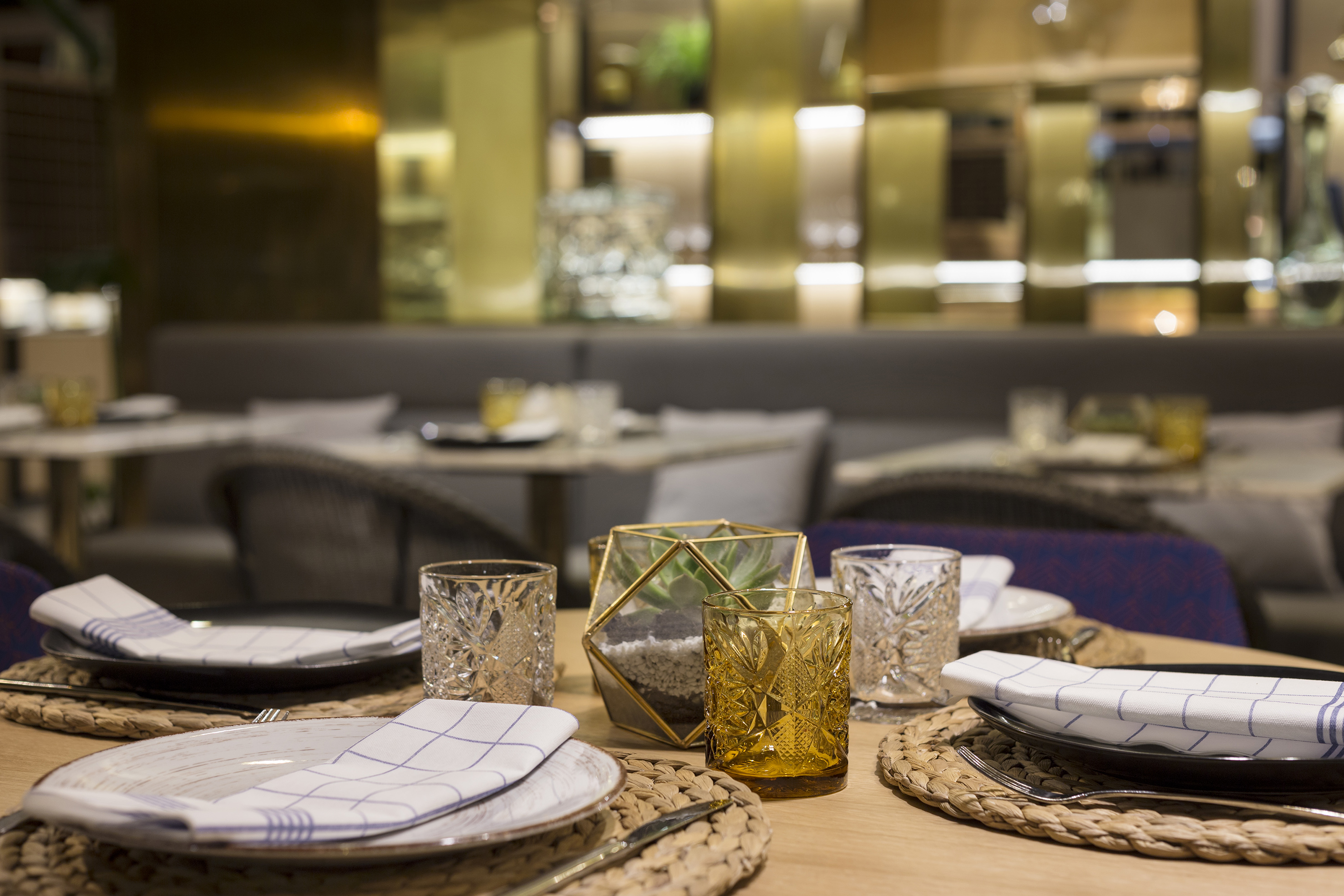 Modern dining table with plates, patterned glasses, and succulent terrarium centerpiece.