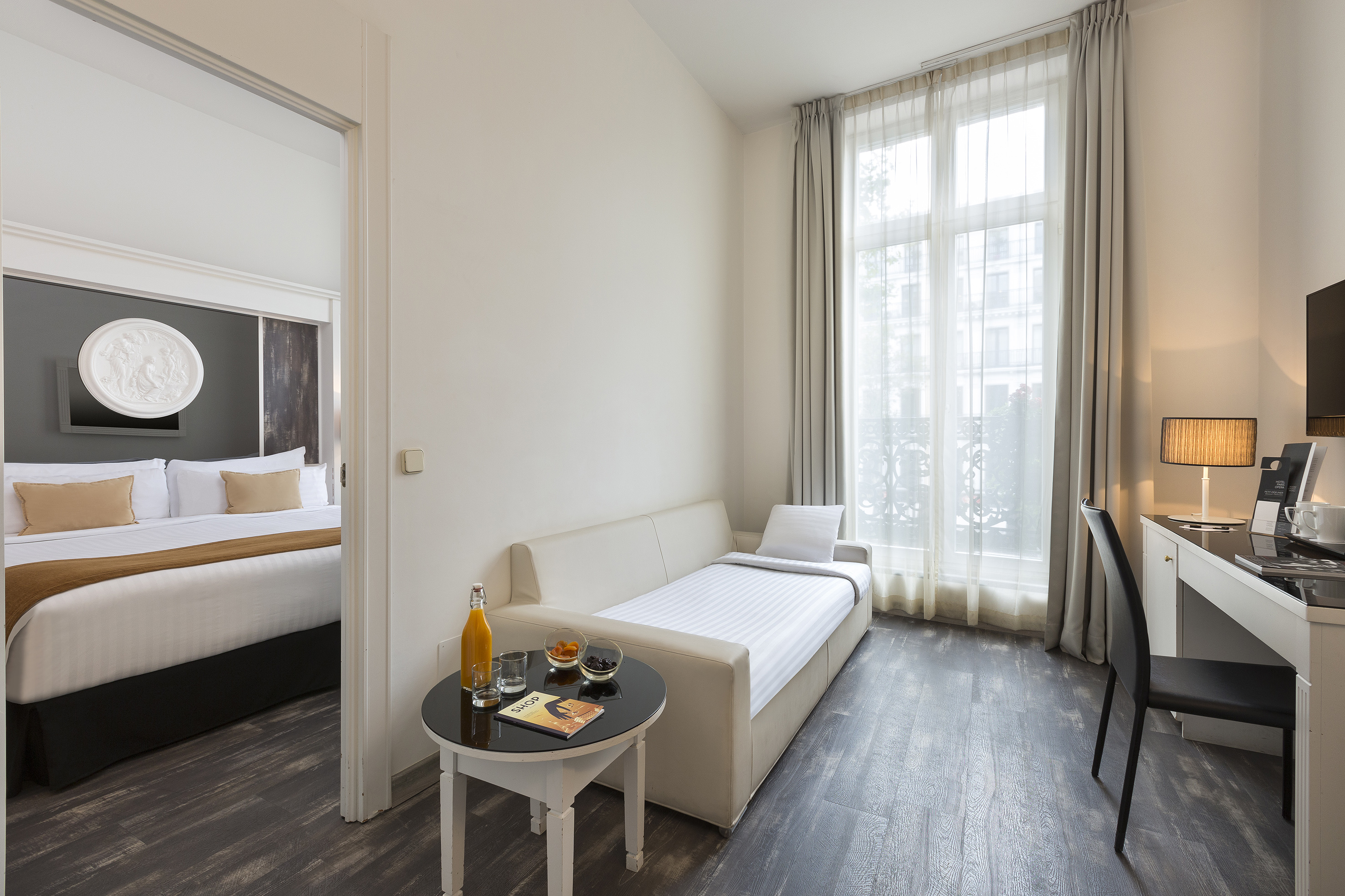 Hotel studio room with sofa bed, desk, and adjoining bedroom.
