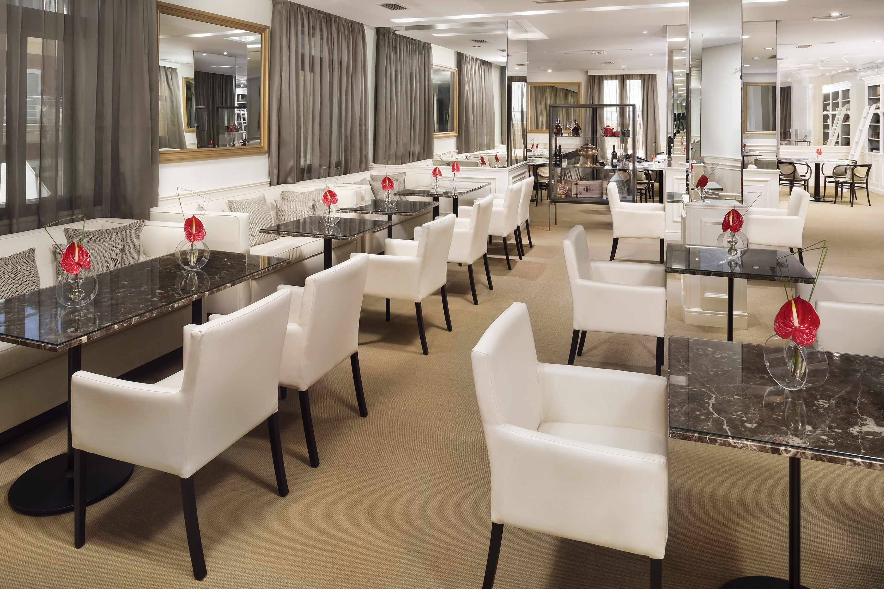 Hotel lounge with white armchairs, dark marble tables, and mirrors.