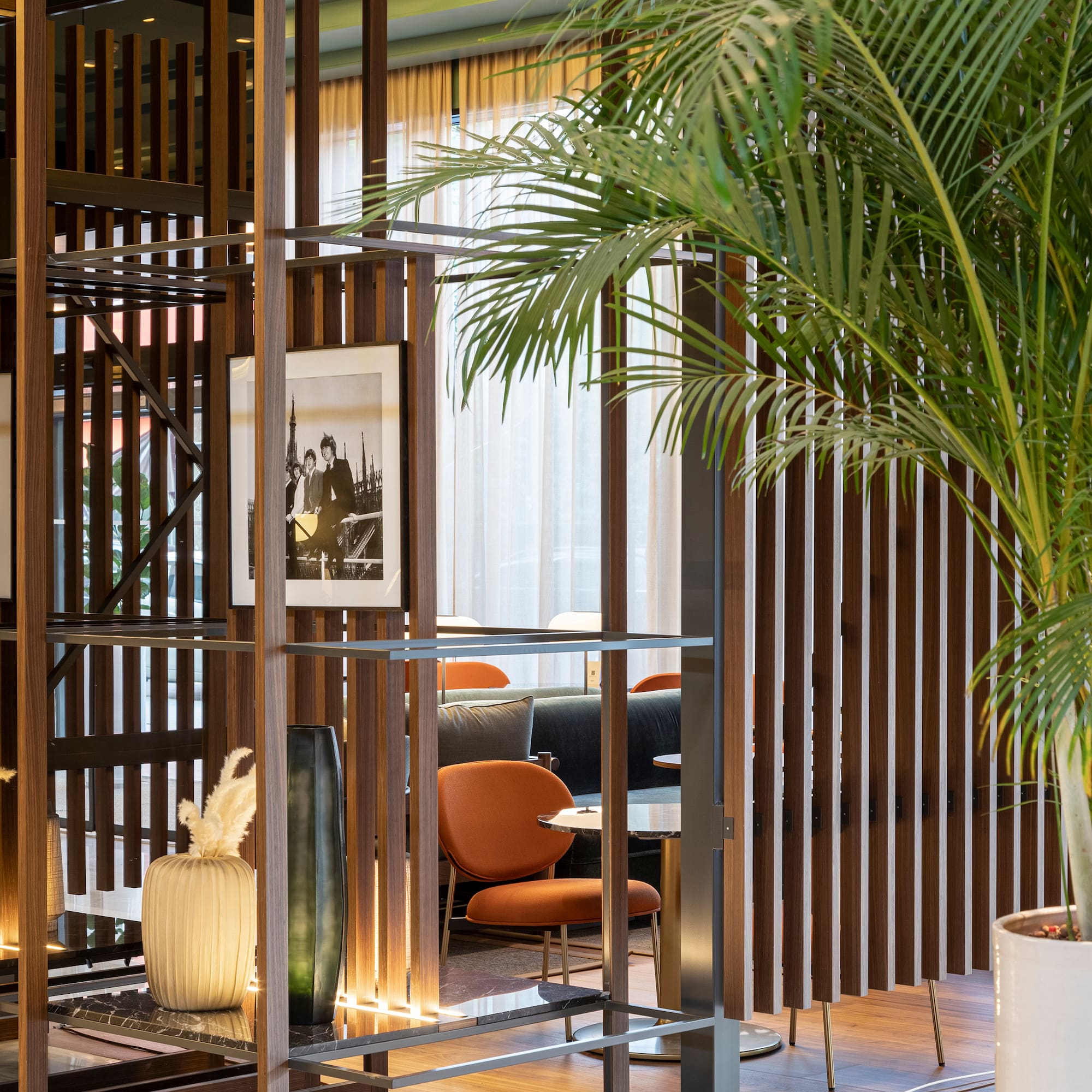 Modern hotel lounge interior with wood divider, palm plant, and stylish seating.