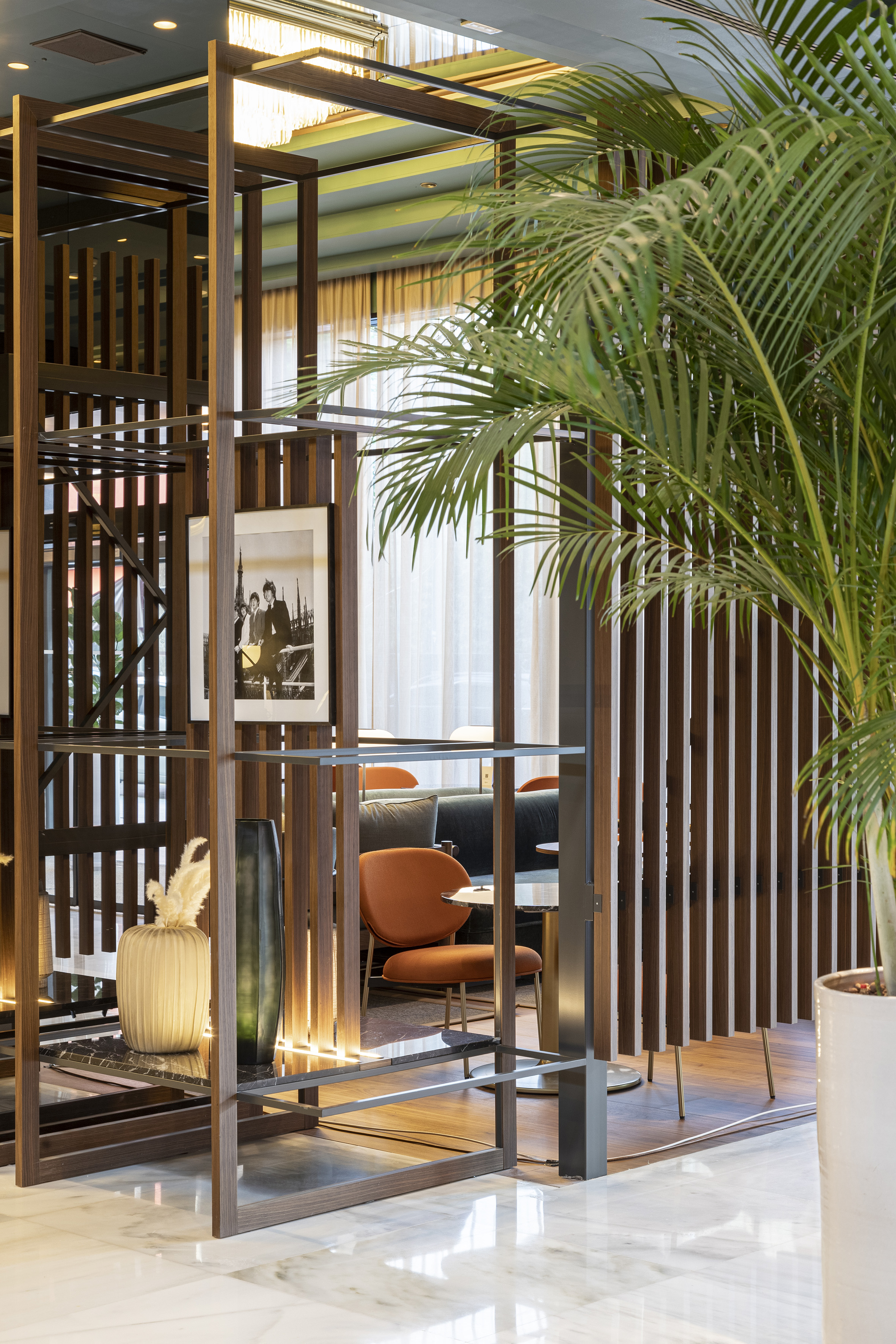 Modern hotel lounge interior with wood divider, palm plant, and stylish seating.