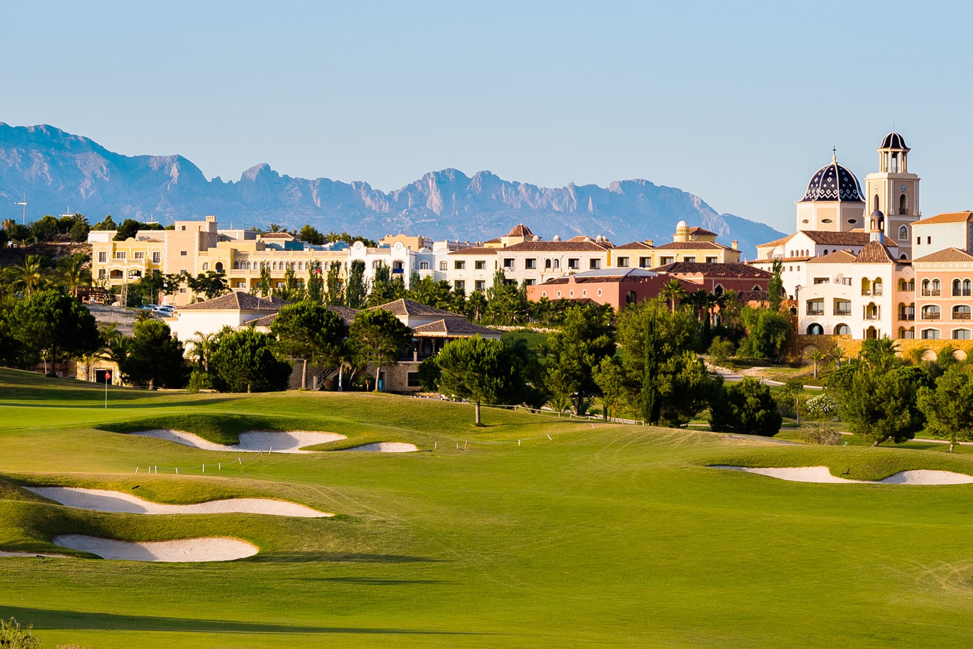 Lush green golf course, Mediterranean resort town, and distant mountains.