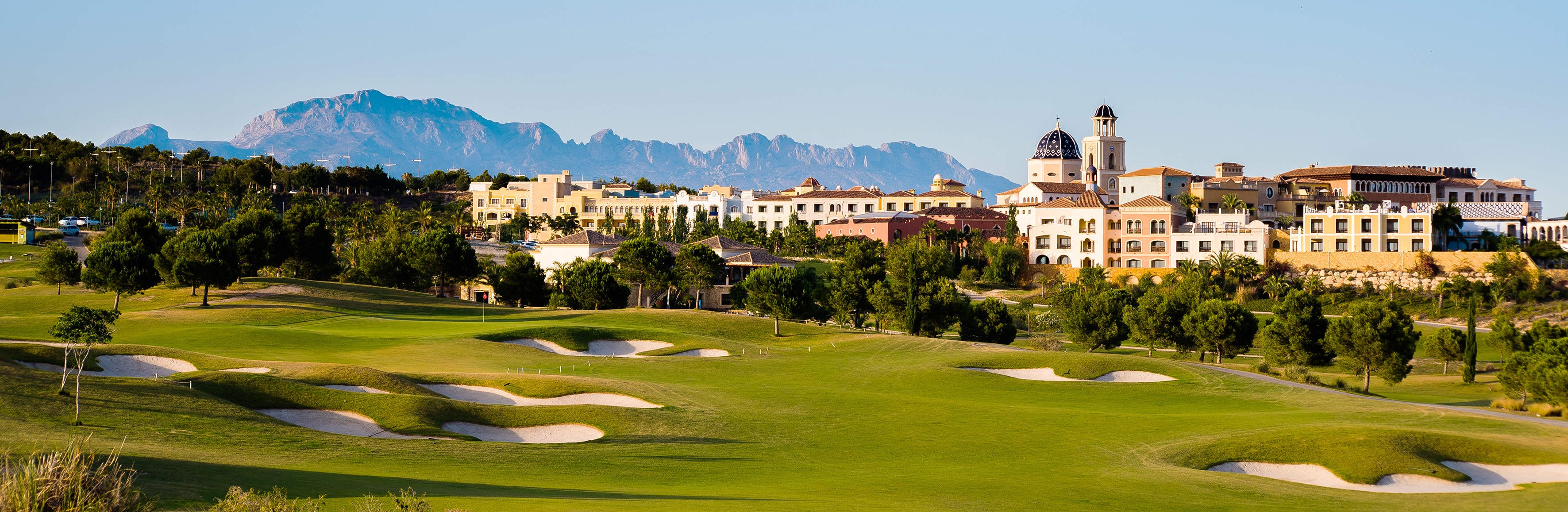 Lush green golf course, Mediterranean resort town, and distant mountains.