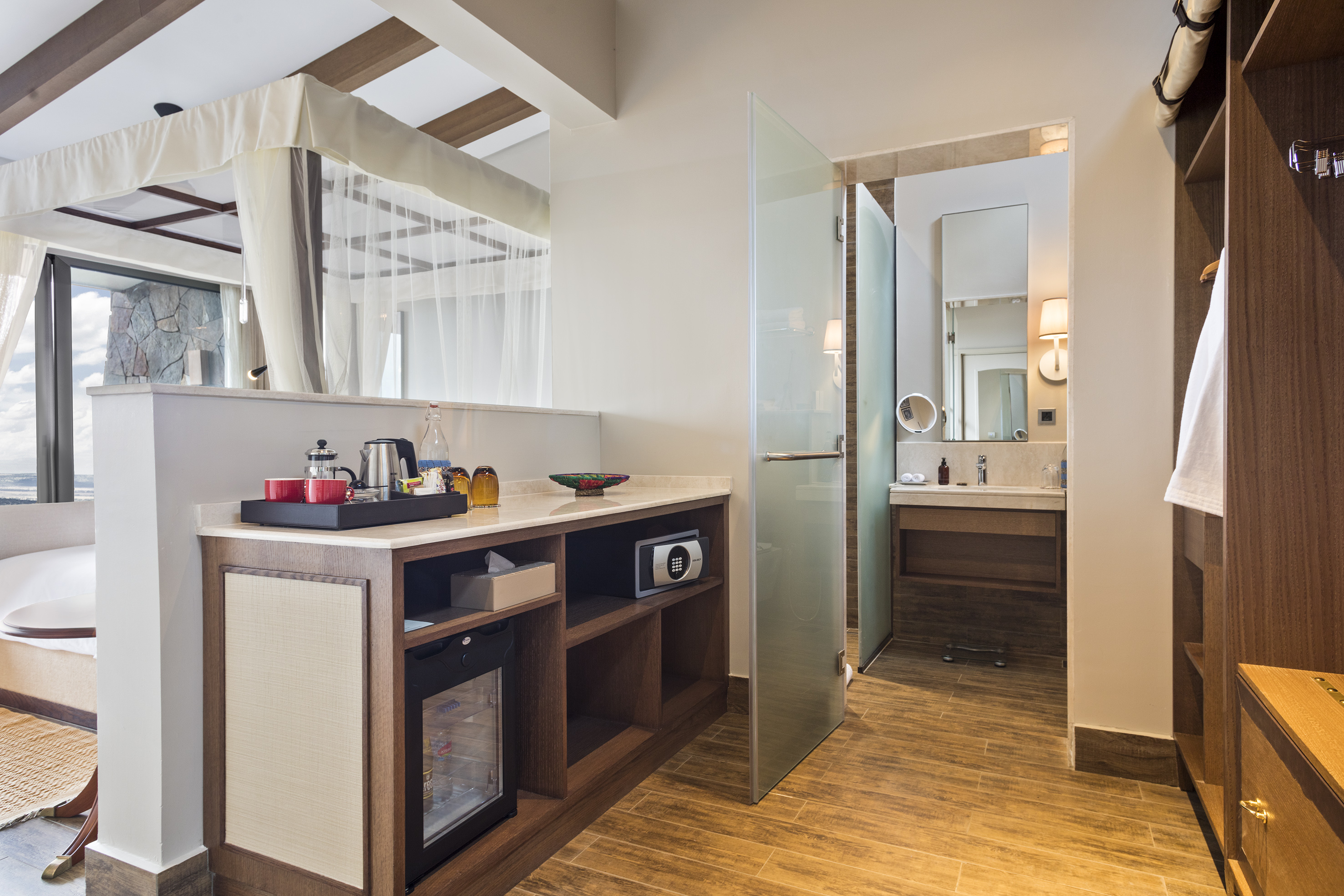Modern hotel suite with four-poster bed, minibar, and open bathroom access.
