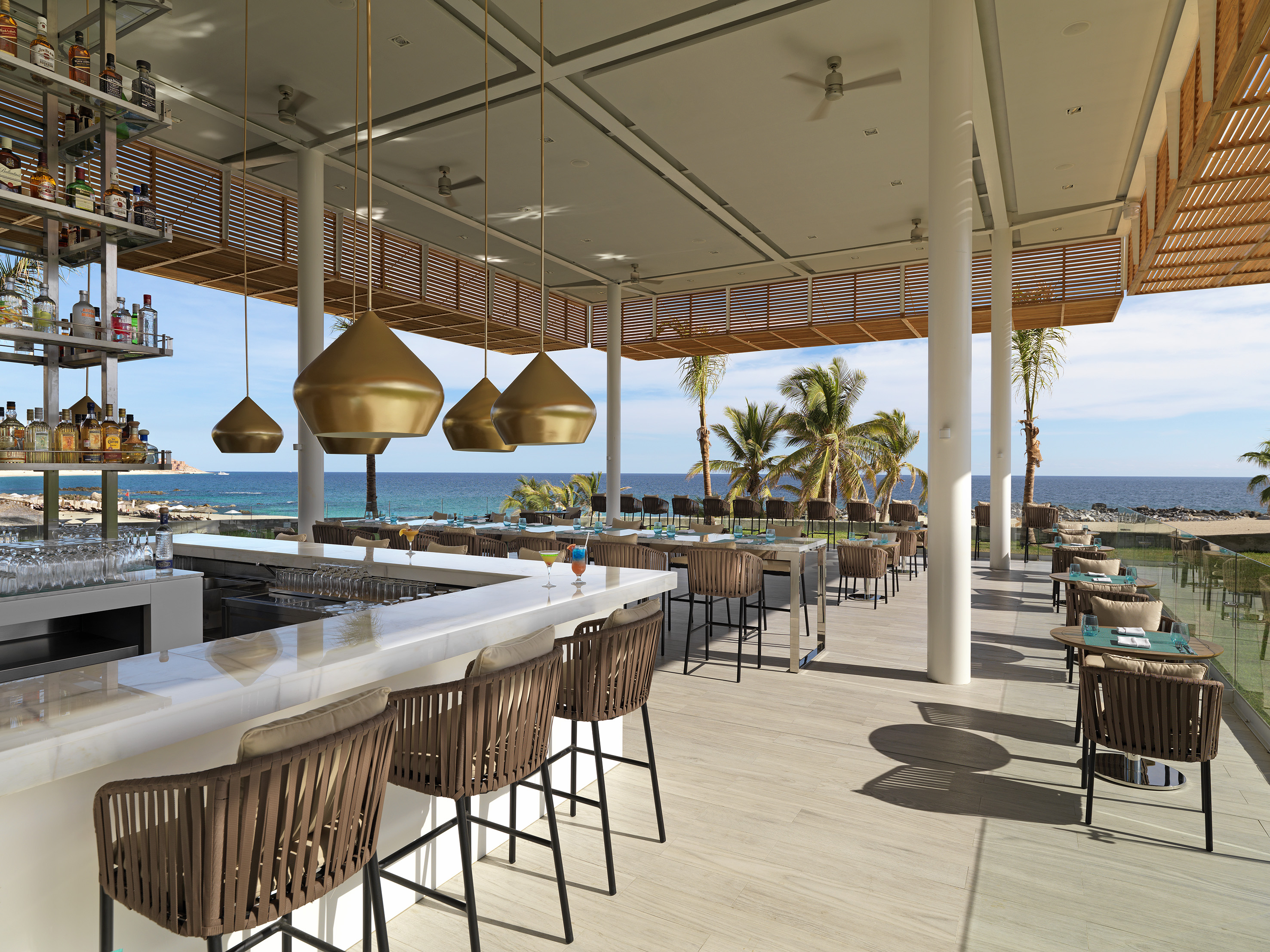 Modern oceanfront bar with gold lights, outdoor dining, and palm trees.